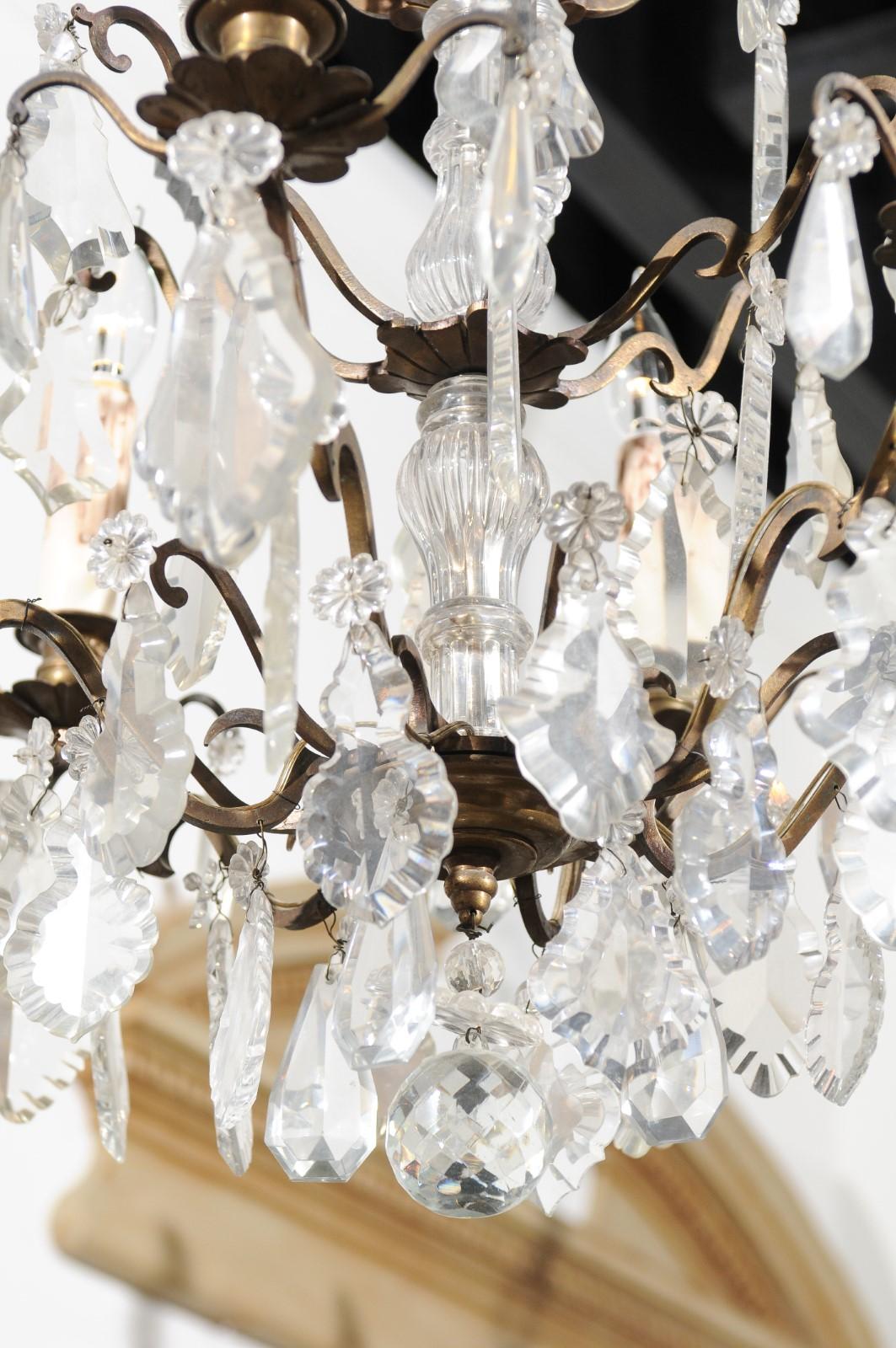 A French Belle-Epoque six-light crystal chandelier from the early 20th century, with brass armature. Born in France during the early years of the 20th century, this exquisite chandelier features a central crystal column, supporting a scrolling brass