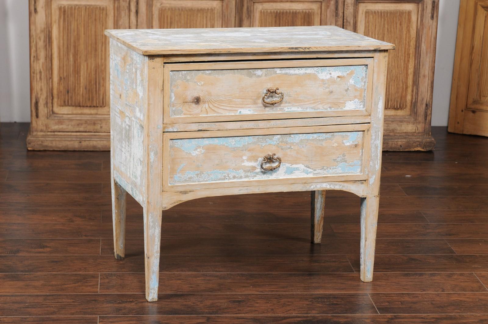 A French two-drawer commode from the early 20th century, with distressed paint and tapered legs. Created in France during the turn of the century, this commode features a rectangular top sitting above two drawers, each fitted with elegant hardware.