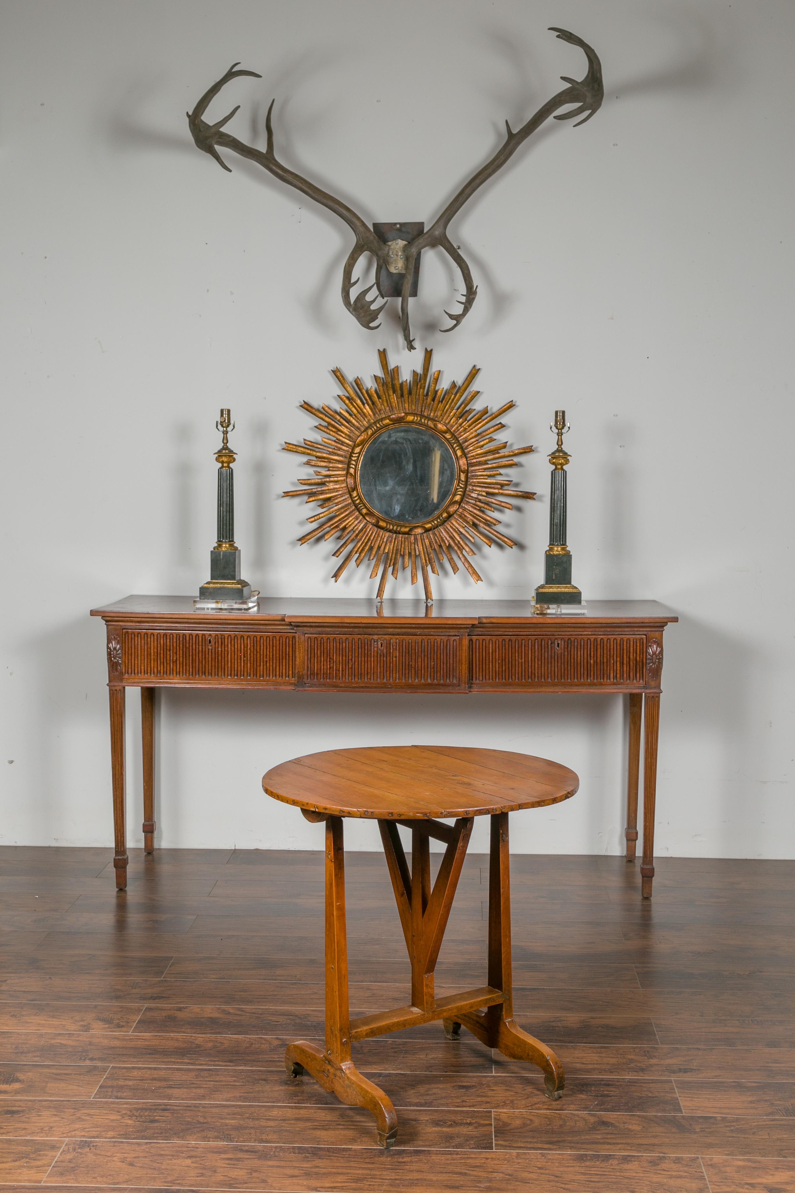 A French walnut wine tasting table from the early 20th century with circular top, trestle base and butterfly wedge. Born in France during the turn of the century, this walnut wine tasting table features a round planked tilt-top, sitting above a