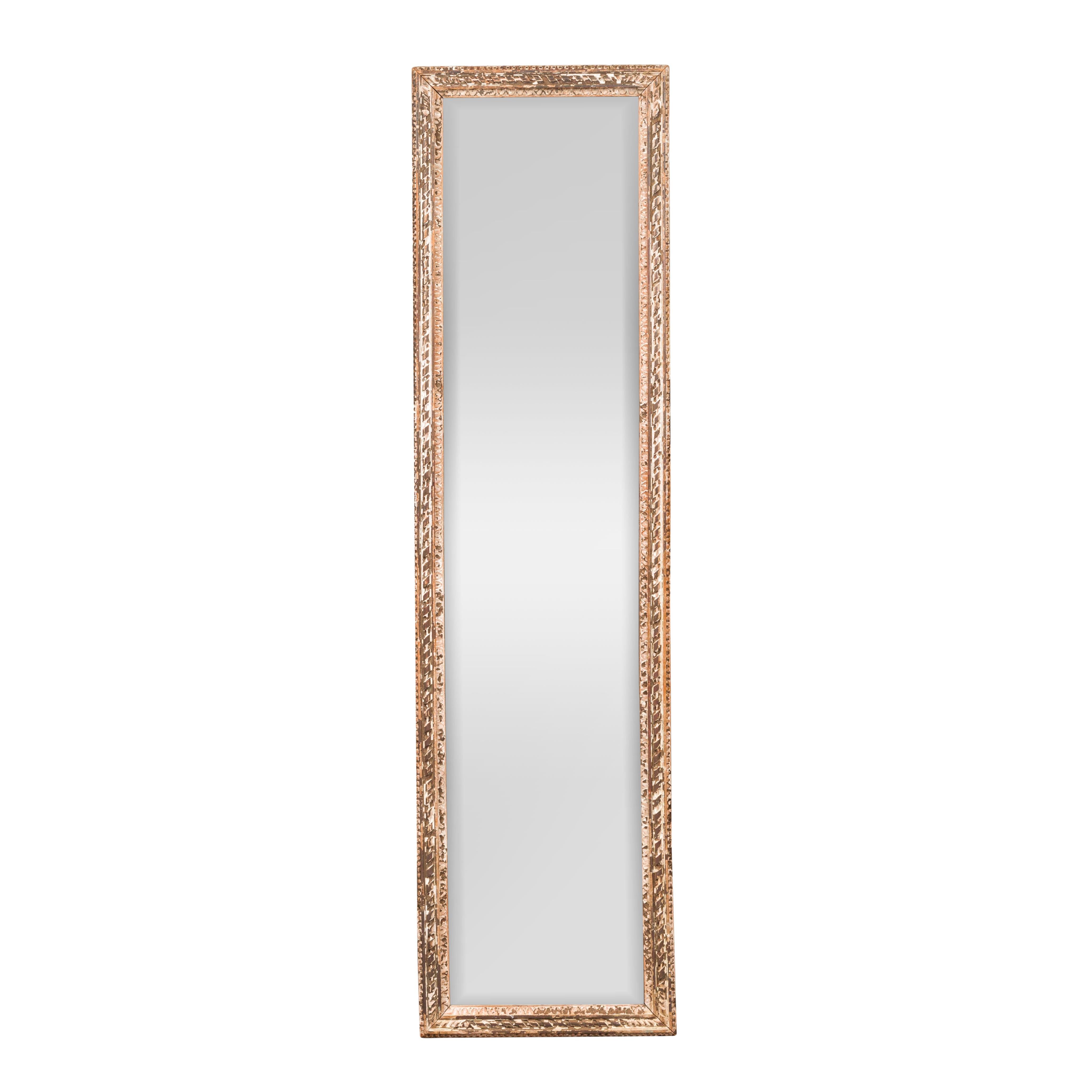 A French tall and narrow carved wooden mirror from the early 20th century, with twisted ribbon motifs and distressed patina. Born in France during the Turn of the Century, this slender mirror features a rectangular frame presenting a nicely