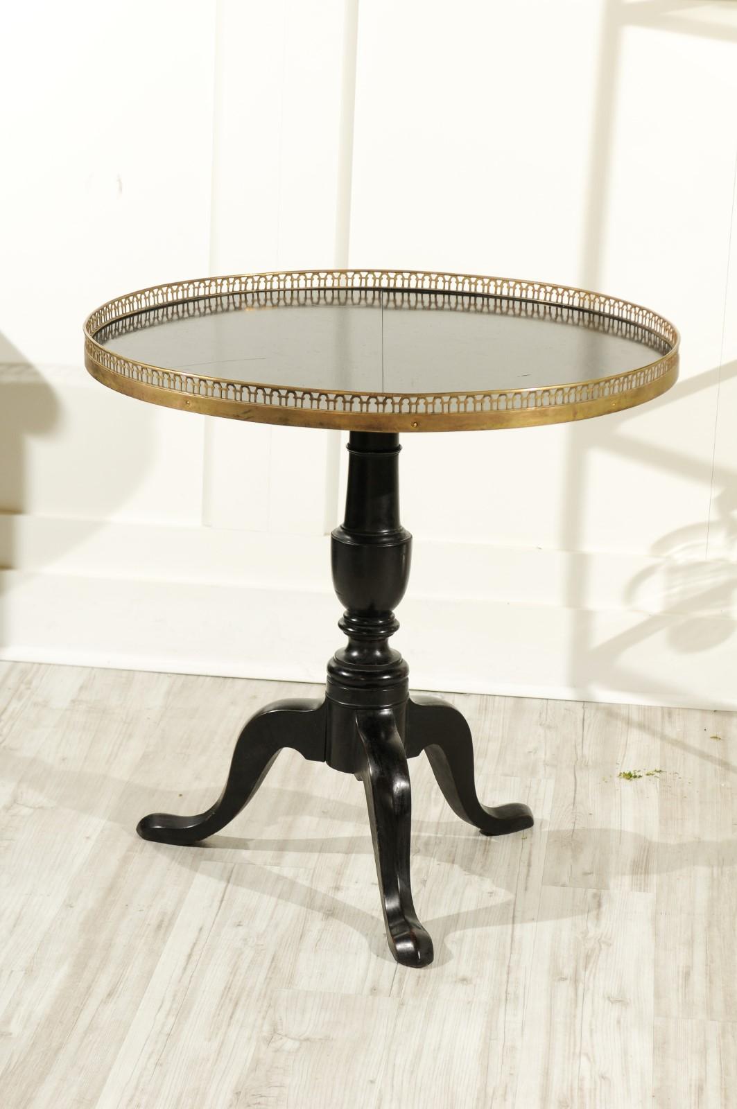 A French black-painted wooden tilt-top table from the early 20th century, with circular pierced brass gallery, turned pedestal and tripod base. This charming French black-painted tilt-top table is a strong counterpoint next to a sofa, in between