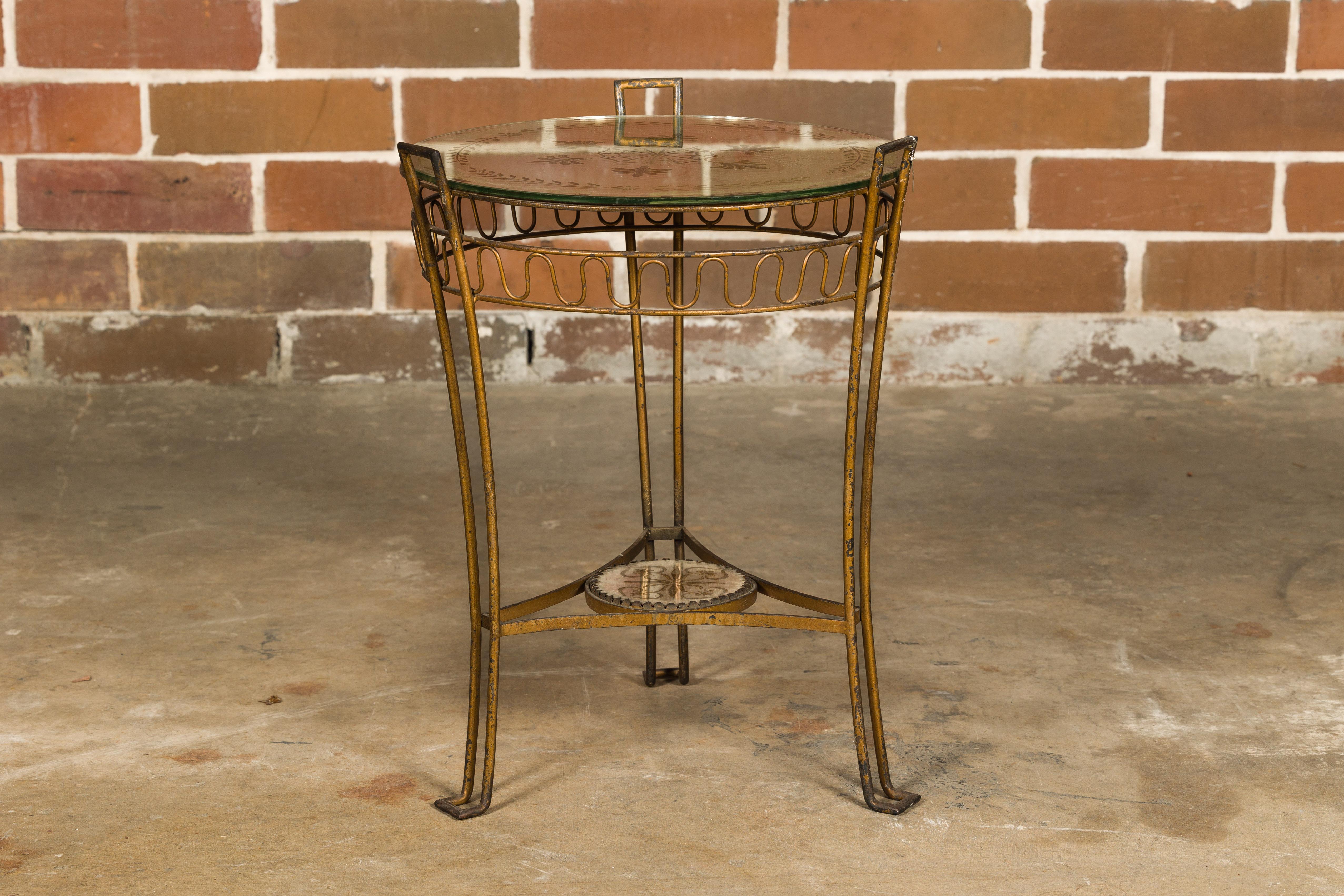 A French gilt iron side table from circa 1920 with etched mirrored top and low shelf. Step into the Parisian elegance of the 1920s with this exquisite French gilt iron side table, featuring an etched mirrored top, a petite low shelf, and three
