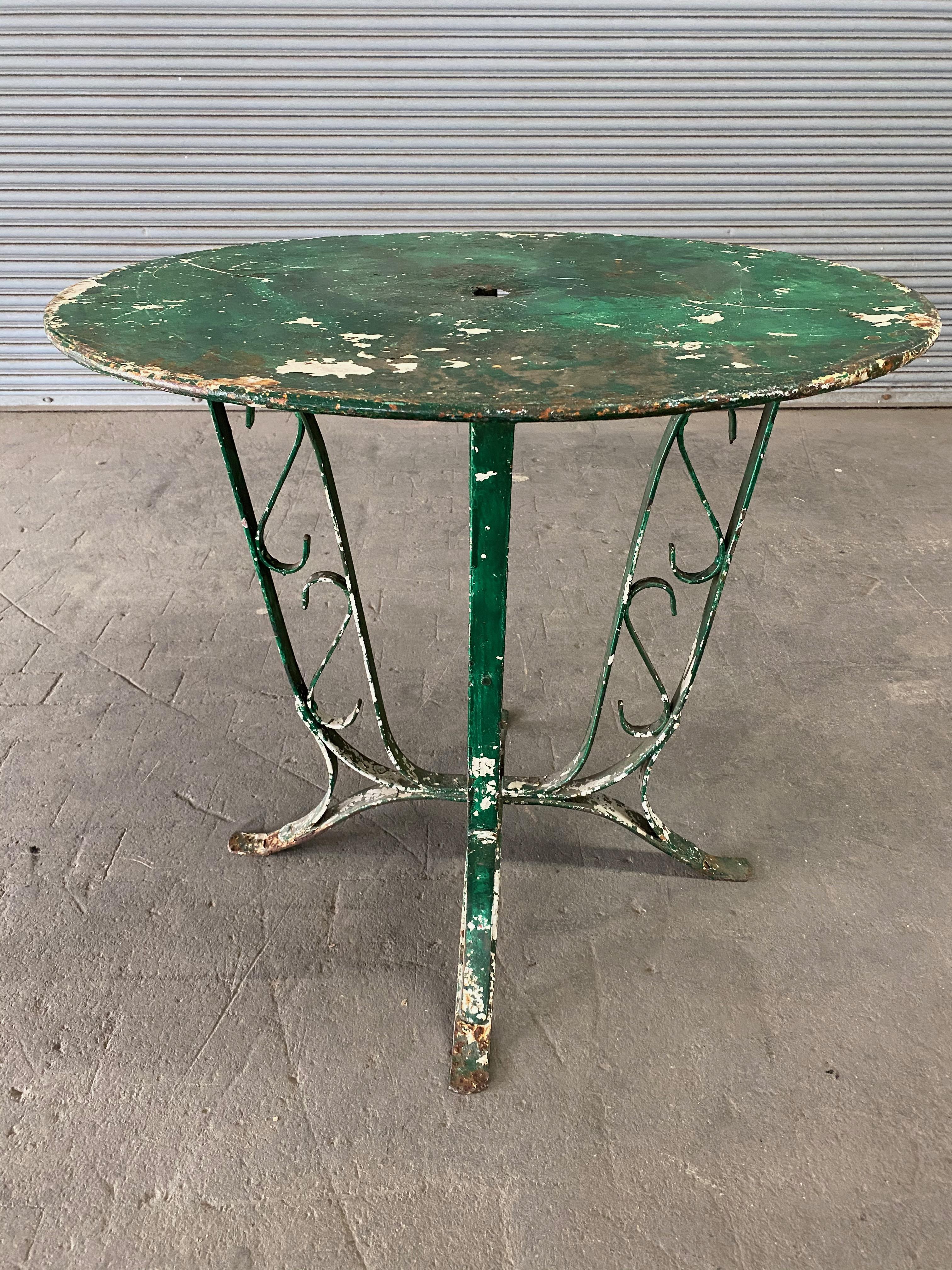Here is a classic French garden table made in the 1920's. This table has been painted many times to preserve the iron and metal. The beautiful green patina probably dates back to the 1950's era. The metal top has an opening to hold an umbrella