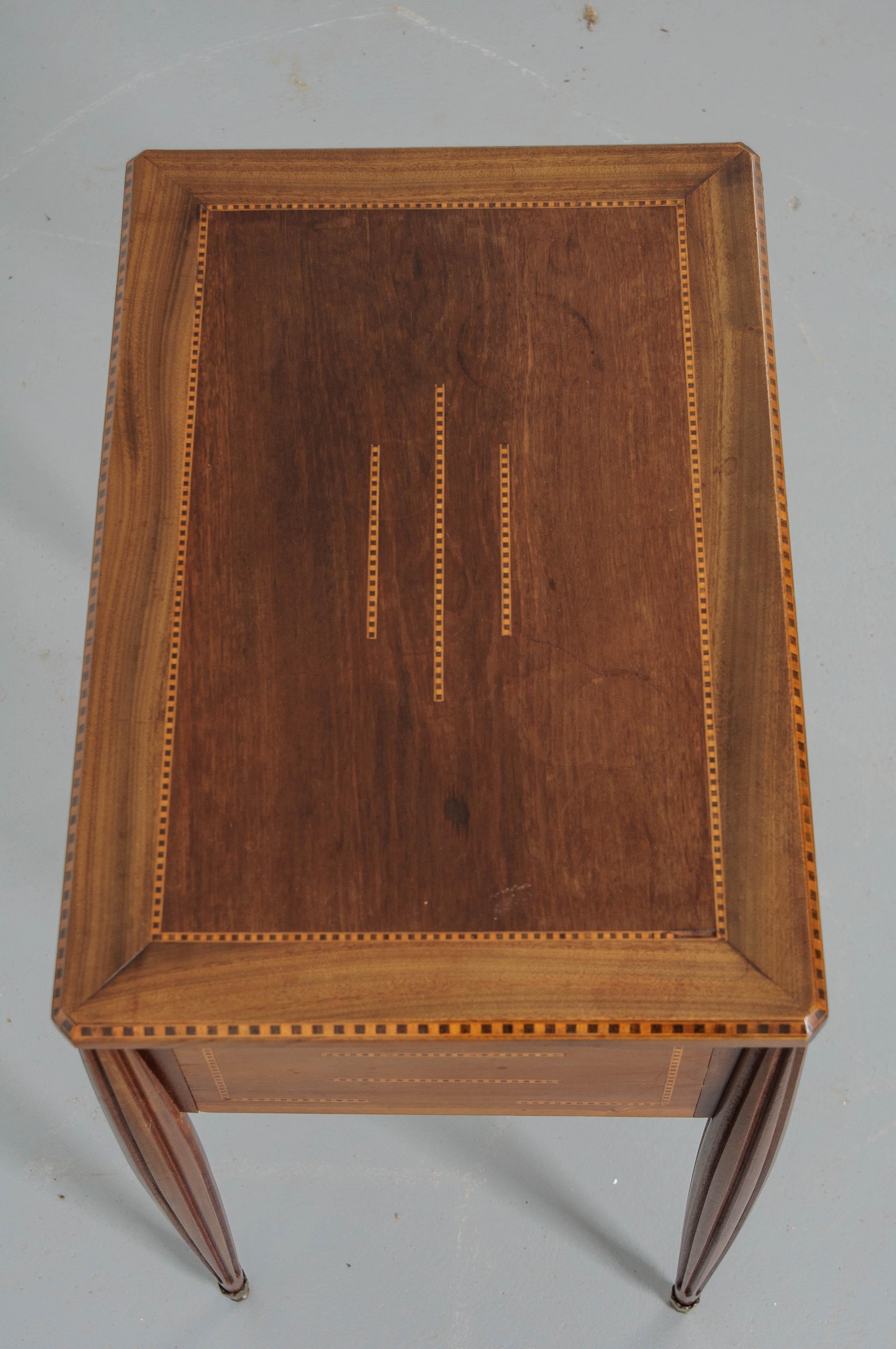 French, Art Deco style, mahogany table with patterned satinwood and ebony inlay on all five surfaces. The tabletop lifts open and is held open with a chain connection, revealing a storage area divided into three parts. A faux drawer front has two