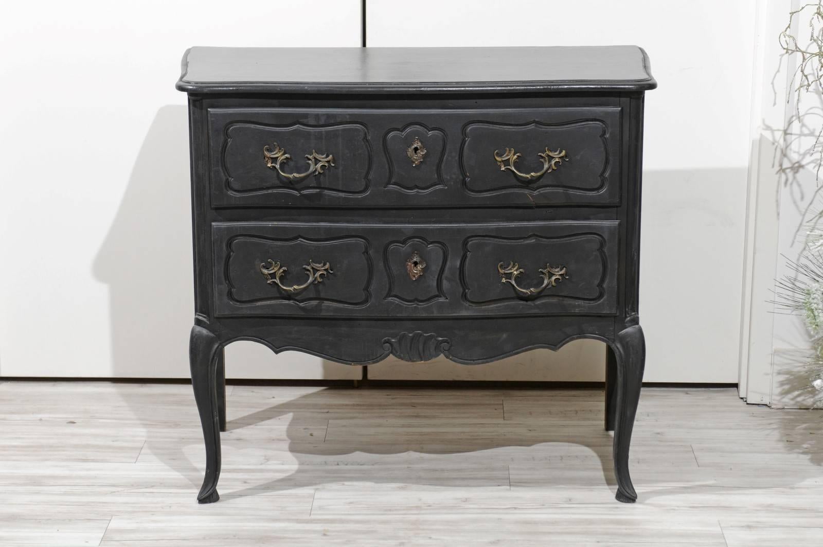 A Northern French black painted Louis XV style two-drawer commode from the early 20th century with Rococo style hardware, scalloped apron and cabriole legs. We are always on the lookout for a smaller commode that will work beautifully as a bedside