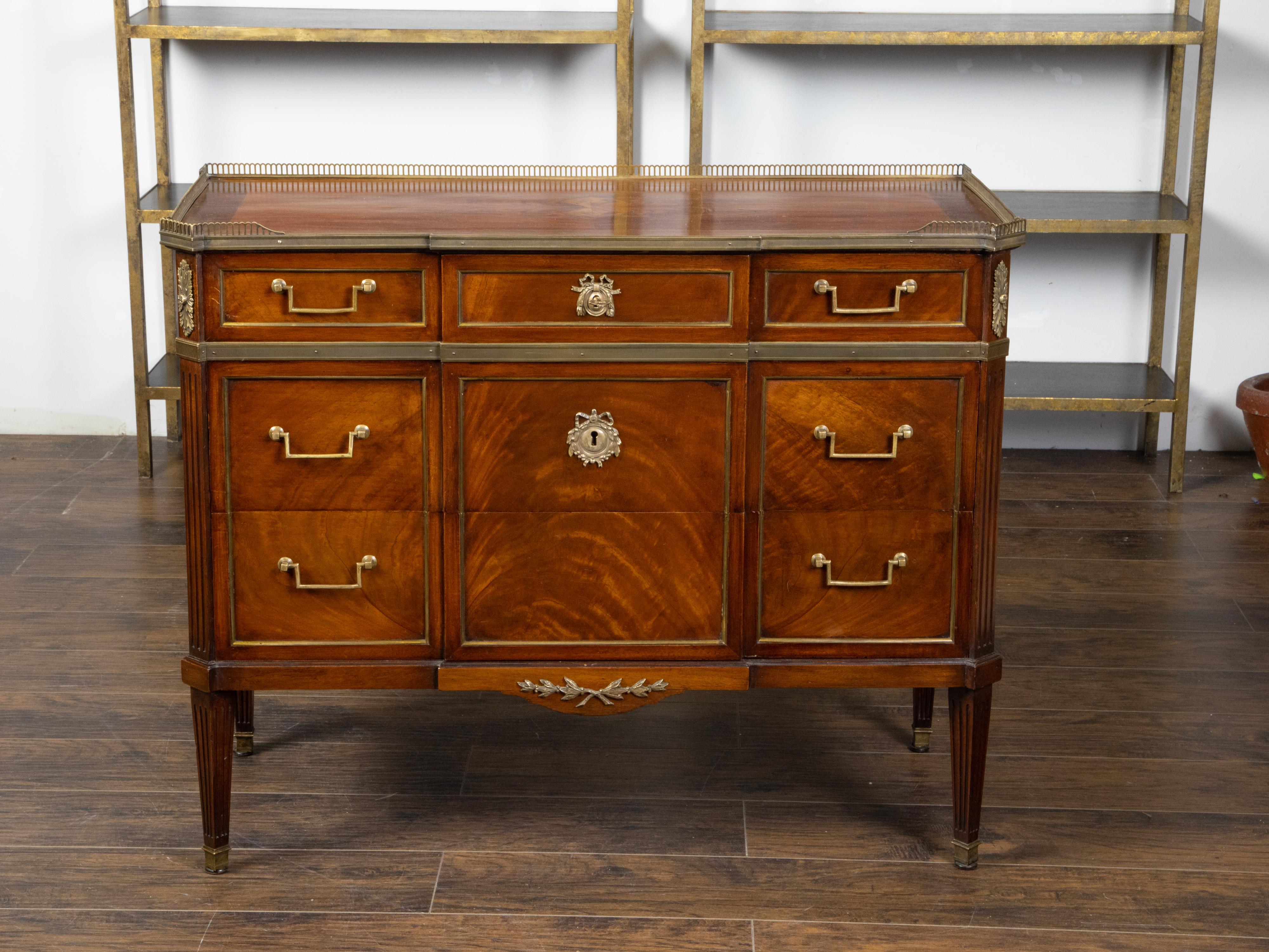 A French mahogany five drawer commode from the early 20th century, with bronze accents. Created in France during the first quarter of the 20th century, this mahogany commode features a rectangular top with butterfly veneer and three-quarter pierced