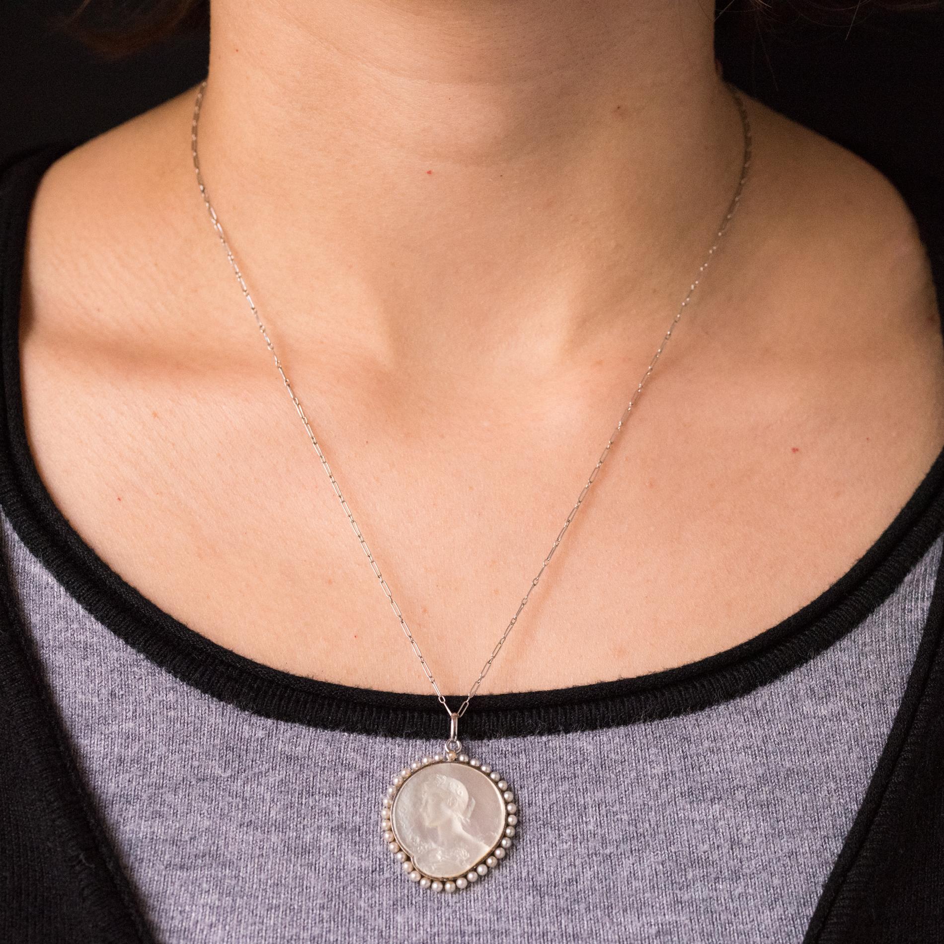 Pendant and its chain in platinum dog head hallmark.
This beautiful antique medal represents the left profile of a woman, engraved on mother-of-pearl, her hair raised with a bouquet of flowers in her hands. All the entourage is in natural pearls.
