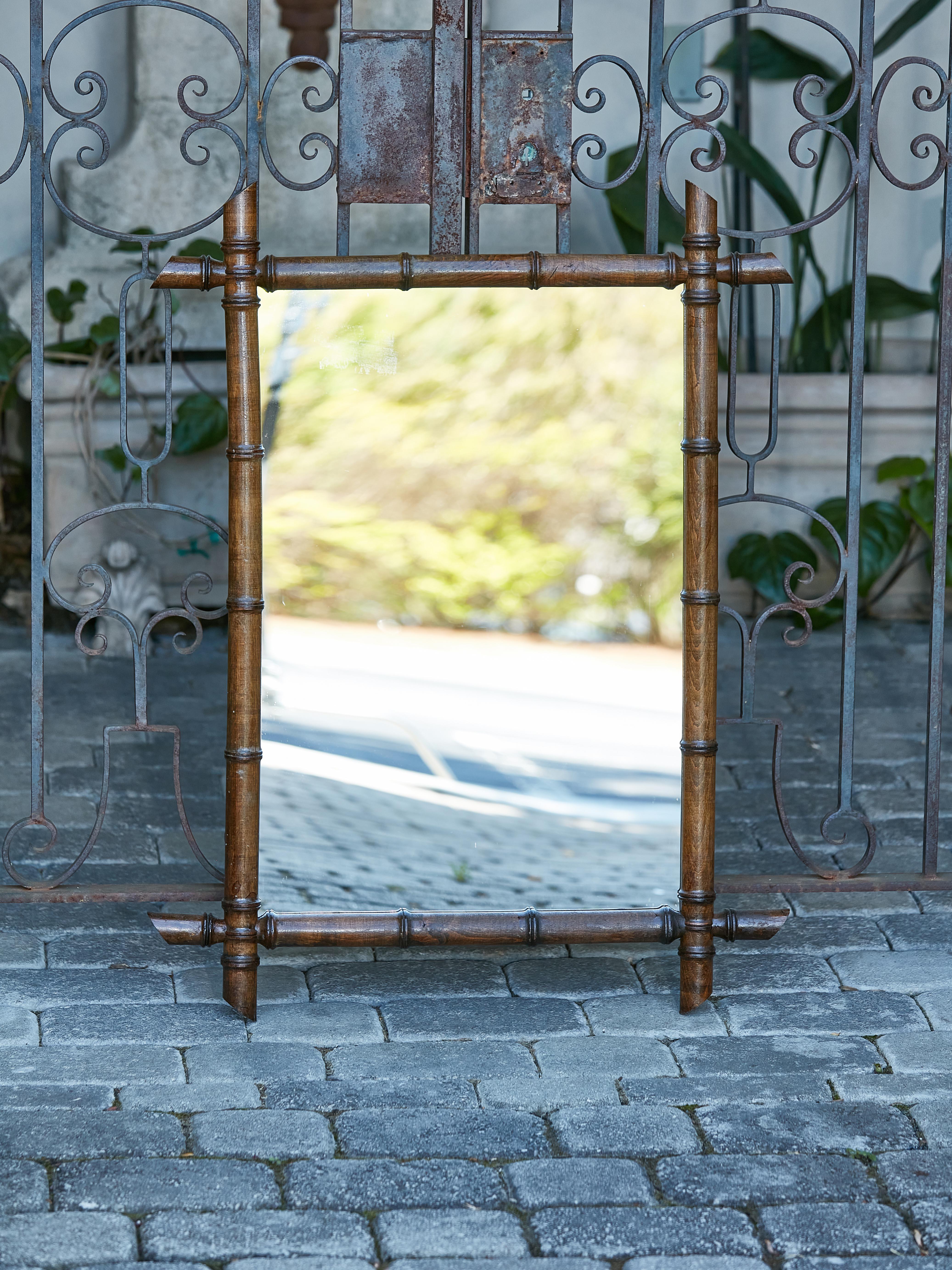 A French rectangular faux-bamboo walnut mirror from the early 20th century, with dark brown patina. Immerse yourself in rustic elegance with this French faux-bamboo walnut mirror from the early 20th century, which effortlessly conjures the charm and