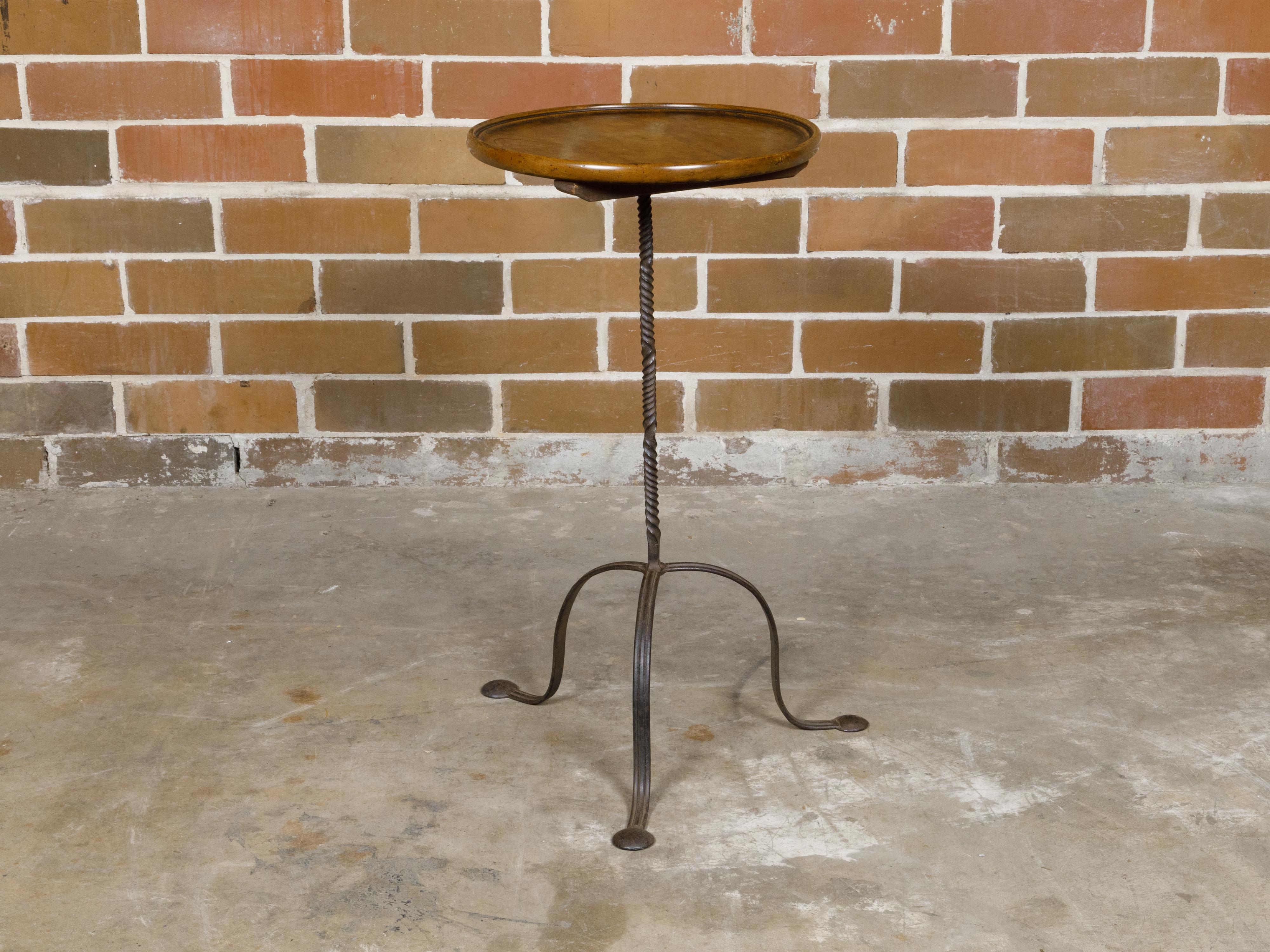 A French side table from circa 1920 with circular wooden tray top and iron base. This charming French side table, dating back to circa 1920, gracefully combines the warmth of a circular wooden tray top with the simple elegance of an iron base. The