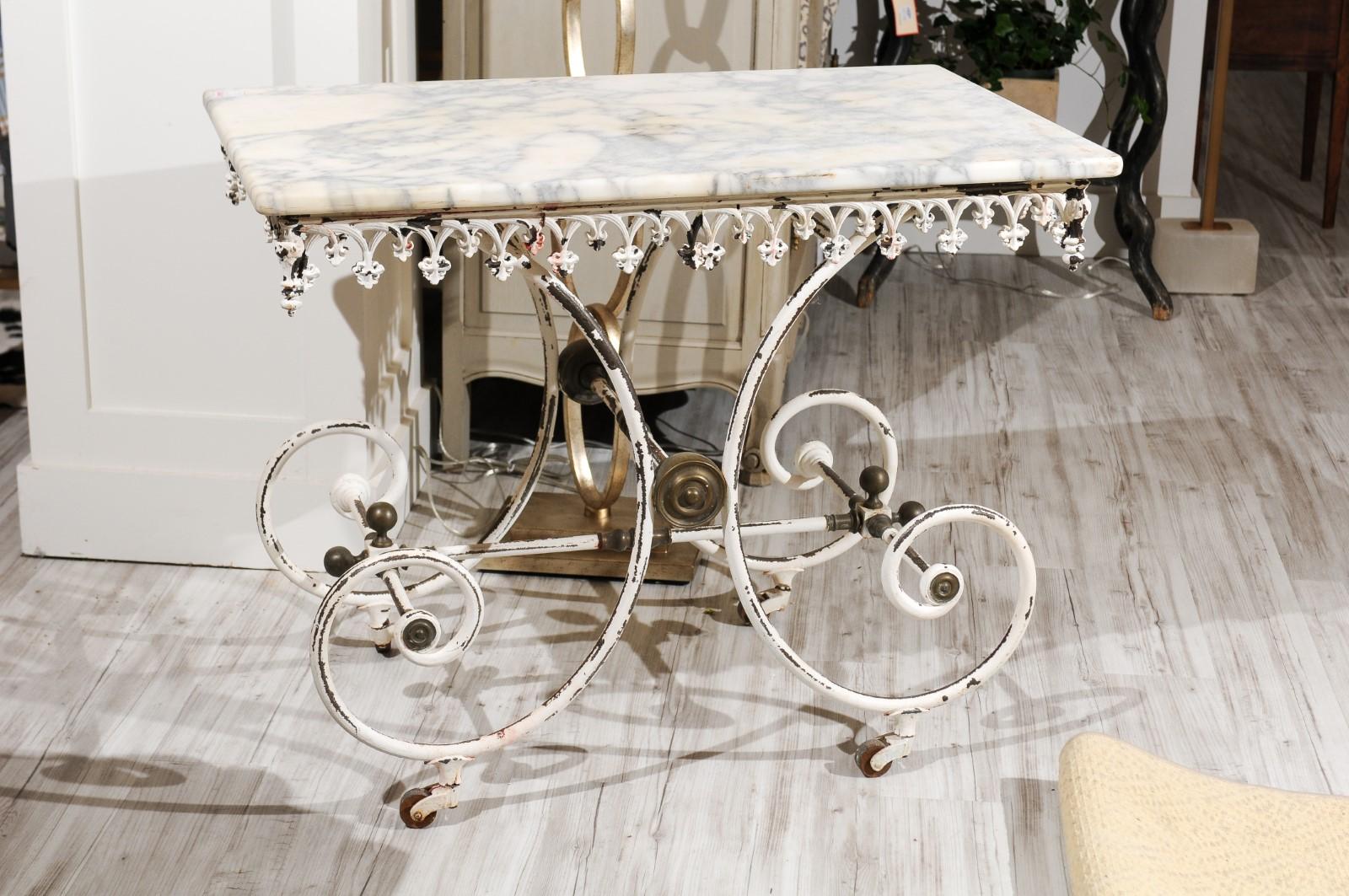 A French white painted iron baker's table on casters from the early 20th century with rectangular marble top, Gothic-inspired apron, scrolling base and brass medallions. The lovely marble top for this French 1920s pastry table is what caught our eye