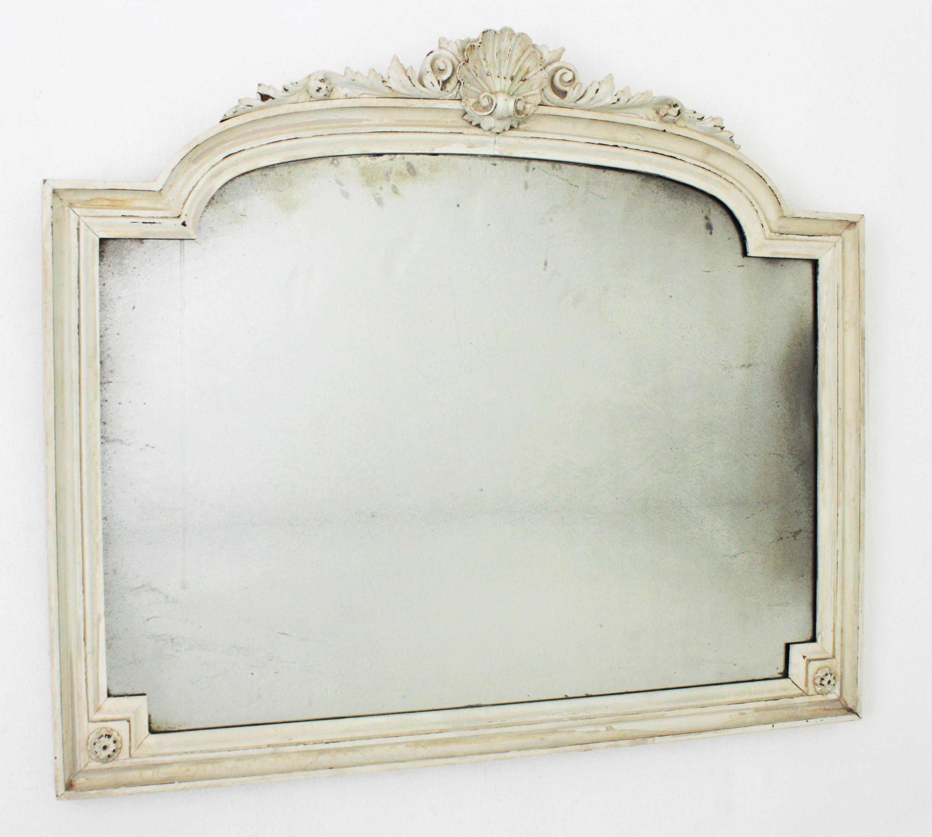 Beautiful arched provençal console mirror with clam shell, floral ornamentations and white patina. France, 1920s.
The carved wood frame is painted in white with accents in ivory and brown color. It wears its original antique glass that show an aged