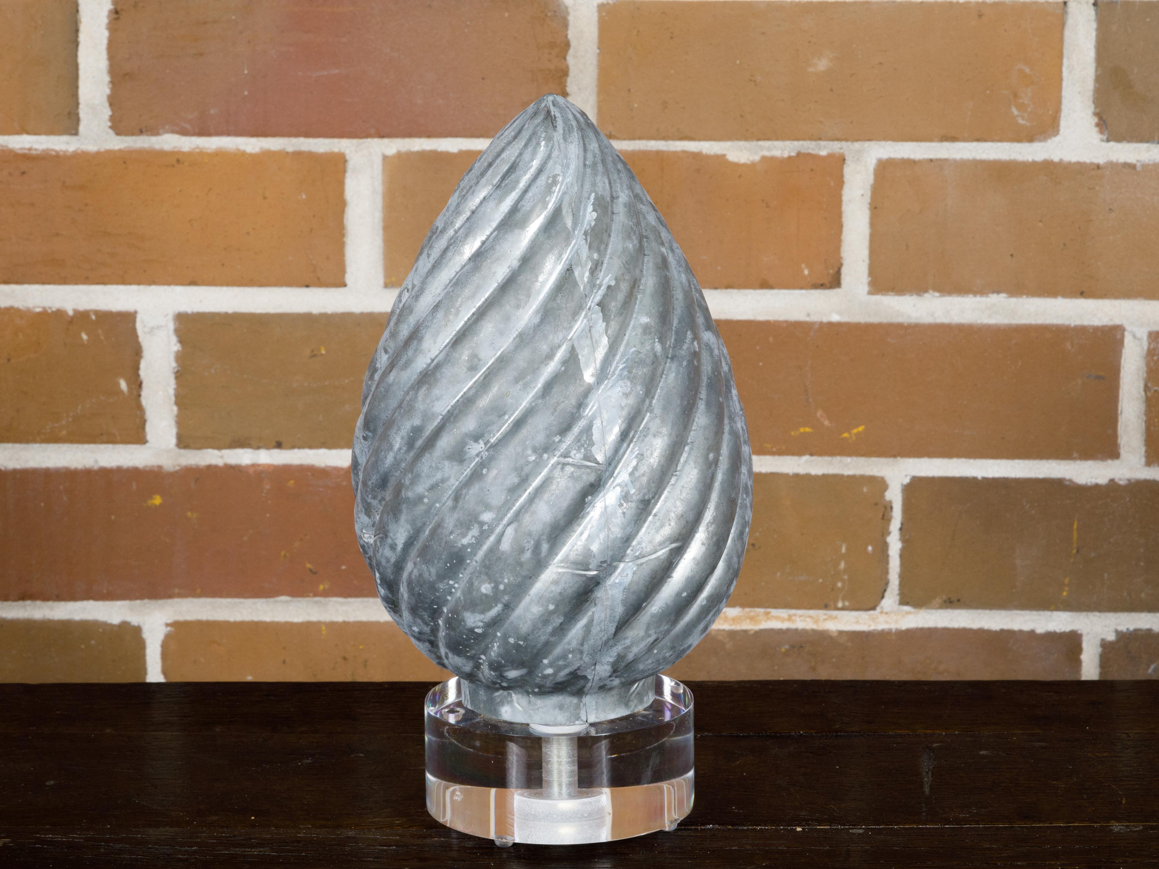 This charming French zinc pine cone shaped decorative object, hailing from circa 1920, merges the allure of nature with the refinement of vintage decor. Elegantly mounted on a circular lucite base, this piece encapsulates the beauty and simplicty of