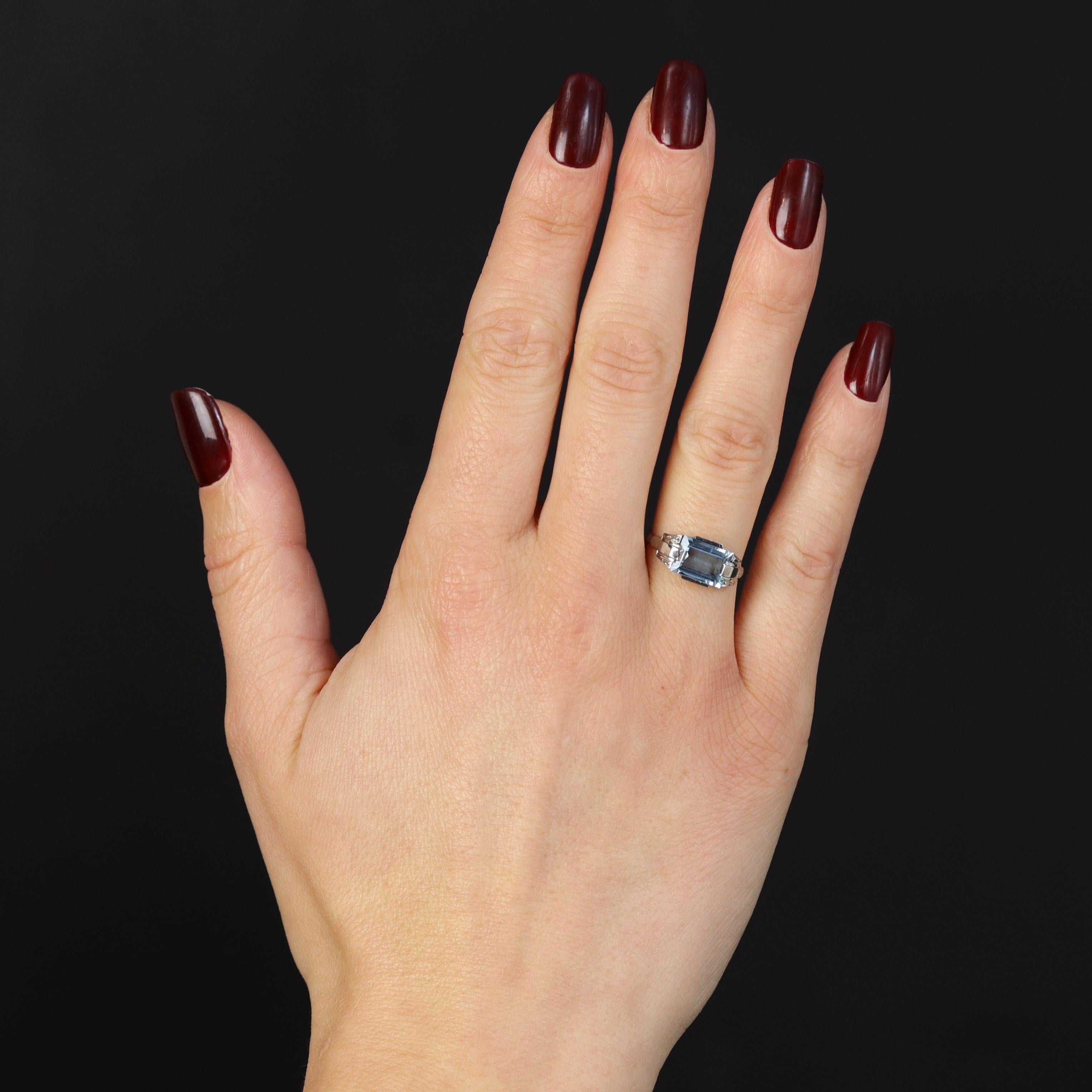 Anello in oro bianco 18 carati, marchio di fabbrica con testa d'aquila.
Luminoso anello antico, la sua montatura geometrica presenta un'acquamarina rettangolare tagliata a gradini sulla parte superiore. È tenuto in posizione su entrambi i lati da