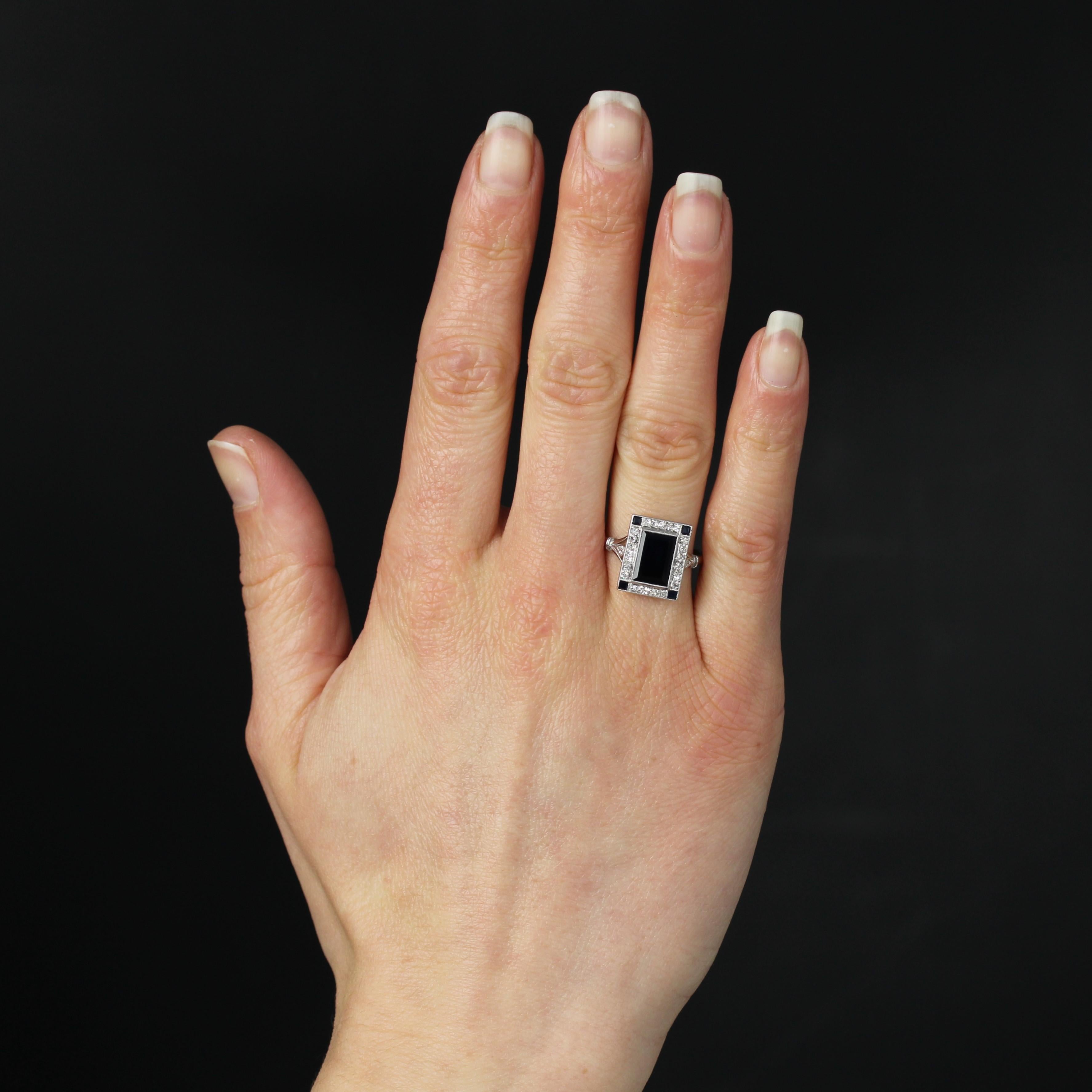 Ring aus Platin, Hundekopfpunze.
Dieser prächtige Art-Déco-Ring hat eine rechteckige Fassung. In der Mitte befindet sich ein tiefblauer, rechteckiger Saphir in einer Fassung aus Diamanten im Antikschliff, die in eine geschlossene Perlenfassung