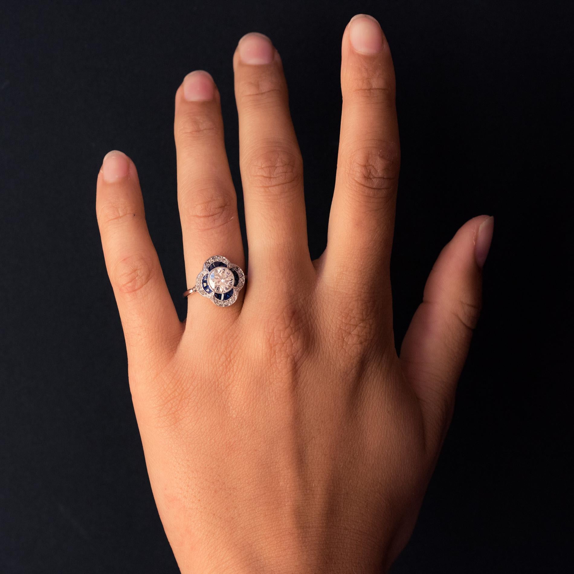 Ring in platinum, dog's head hallmark.
Sublime art deco ring, its clover-shaped setting is set in the center with a modern brilliant-cut diamond in a millegrain bezel setting. Three calibrated sapphires and five 8/8 cut diamonds are set in each