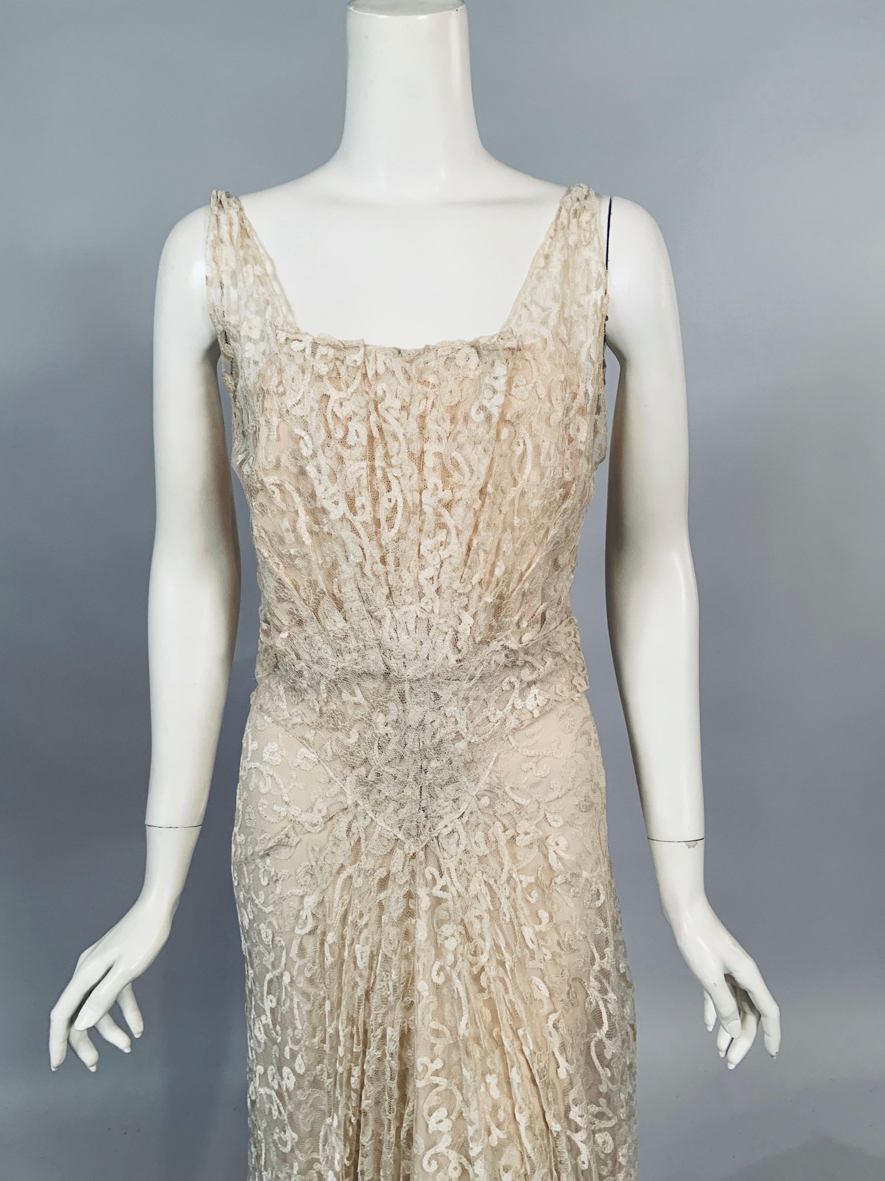 Feminine ivory cotton lace in a tone on tone swirling design is used for this 1930's bias cut evening gown and
matching slip with the Biaolo, Paris label. The dress has narrow straps, a pleated bodice with a square neckline in front and a V shaped
