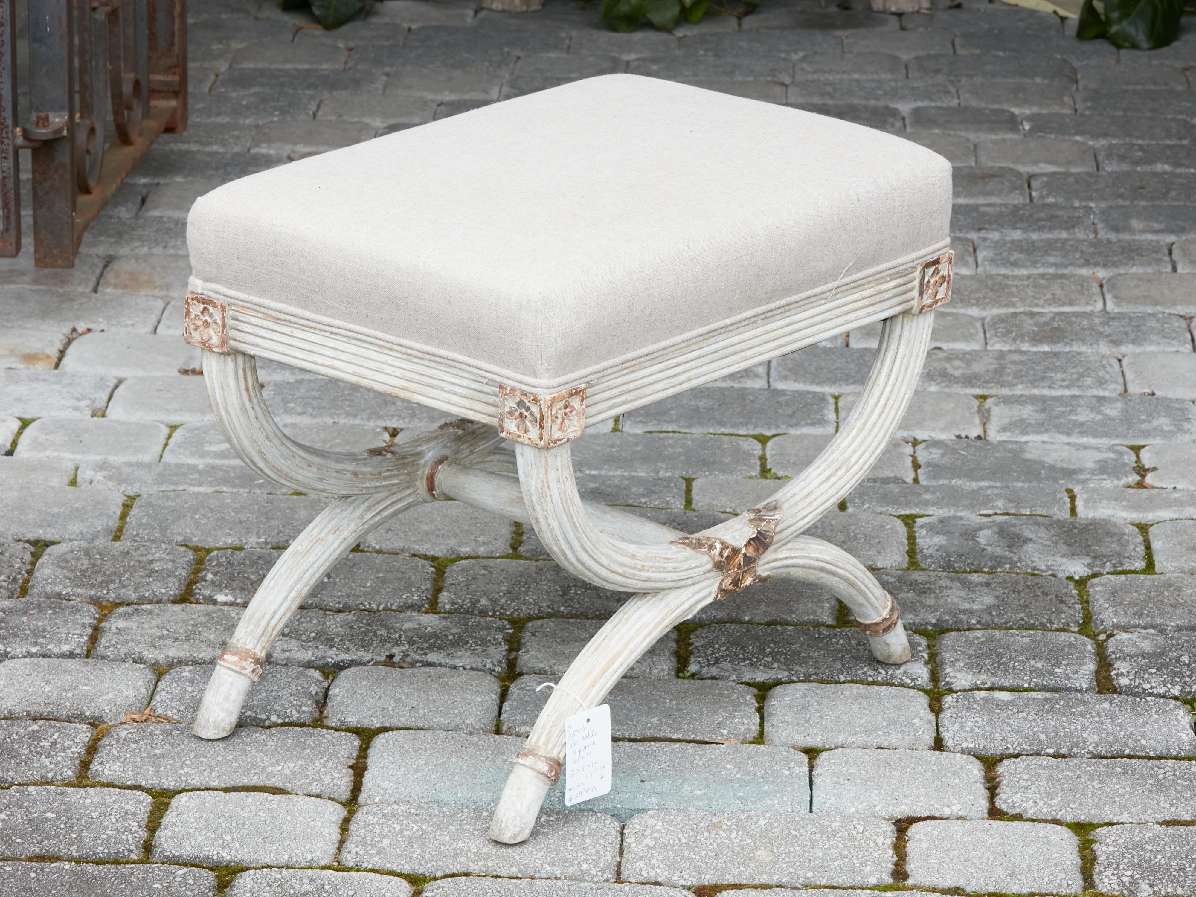 A French curule painted wood stool from the early 20th century, with double X-Form base and new upholstery. Created in France during the second quarter of the 20th century, this curule stool features a rectangular seat newly reupholstered with a