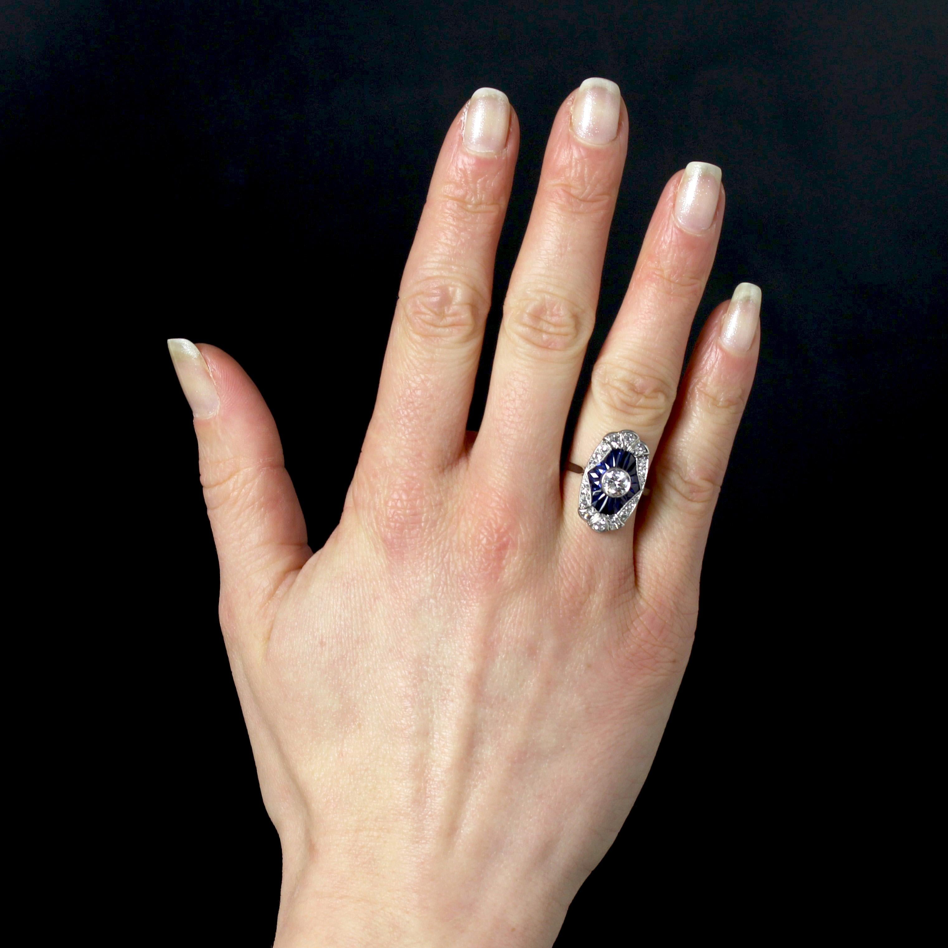 Ring in platinum, mascaron hallmark.
A voluminous Art Deco ring, its flat setting is adorned with 8/8-cut diamonds all around, and a brilliant-cut antique diamond in the center. Calibrated sapphires radiate around the central diamond. The basket is