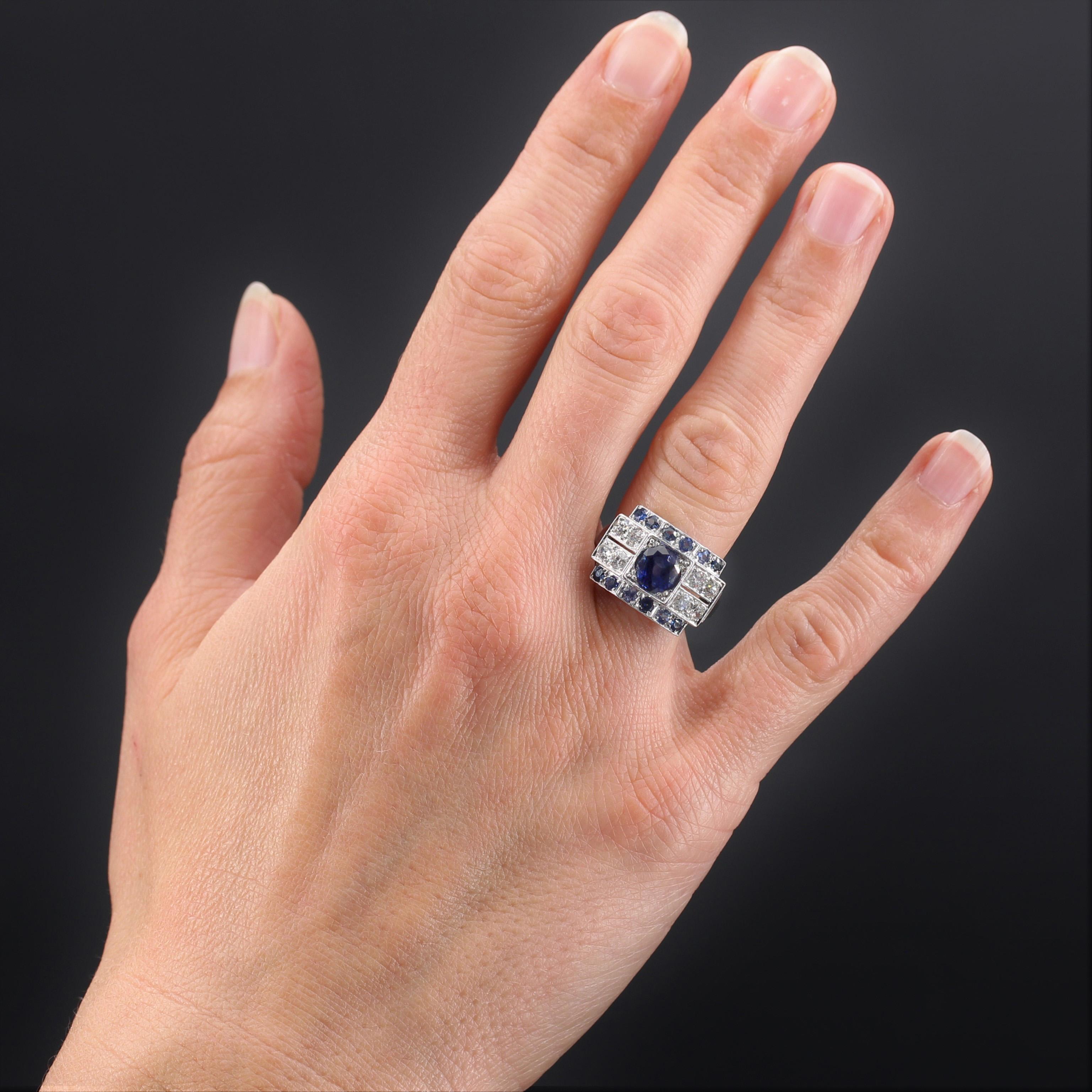 Ring in 18 karat white gold.
Magnificent art deco ring it is formed of a geometrical and curved setting to follow the shape of the finger. A round sapphire, of an intense blue, is set on top, framed by 2 lines of 6 round sapphires, and shouldered by