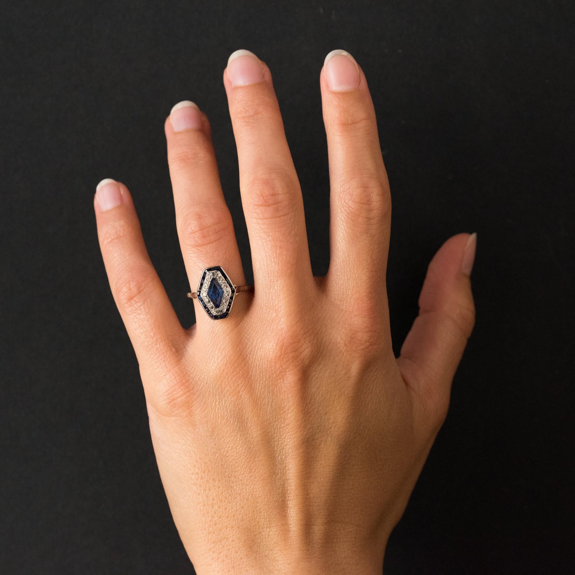 Ring in platinum and 18 karats white gold, eagle's head hallmark.
This charming art deco ring with hexagonal lines is adorned with a blue lozenge sapphire surrounded by rose- cut diamonds. It is bordered on all its circumference by blue gems.
Height