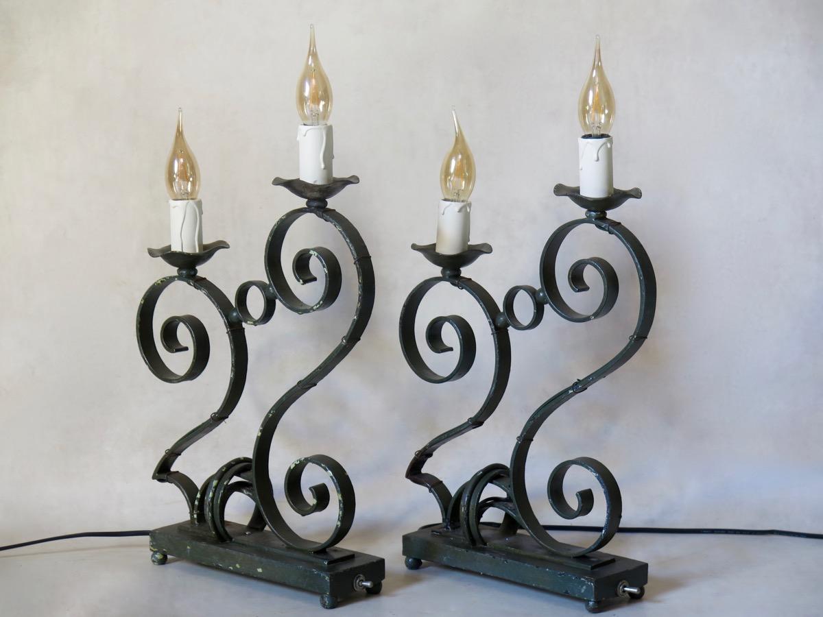 French 1930s wrought-iron table lamps with a dark matte-green finish. The lamps have a chrome switch on the side of the rectangular bases. They are fairly heavy. The lamps are quite unusual in that they combine a sturdy industrial quality with a