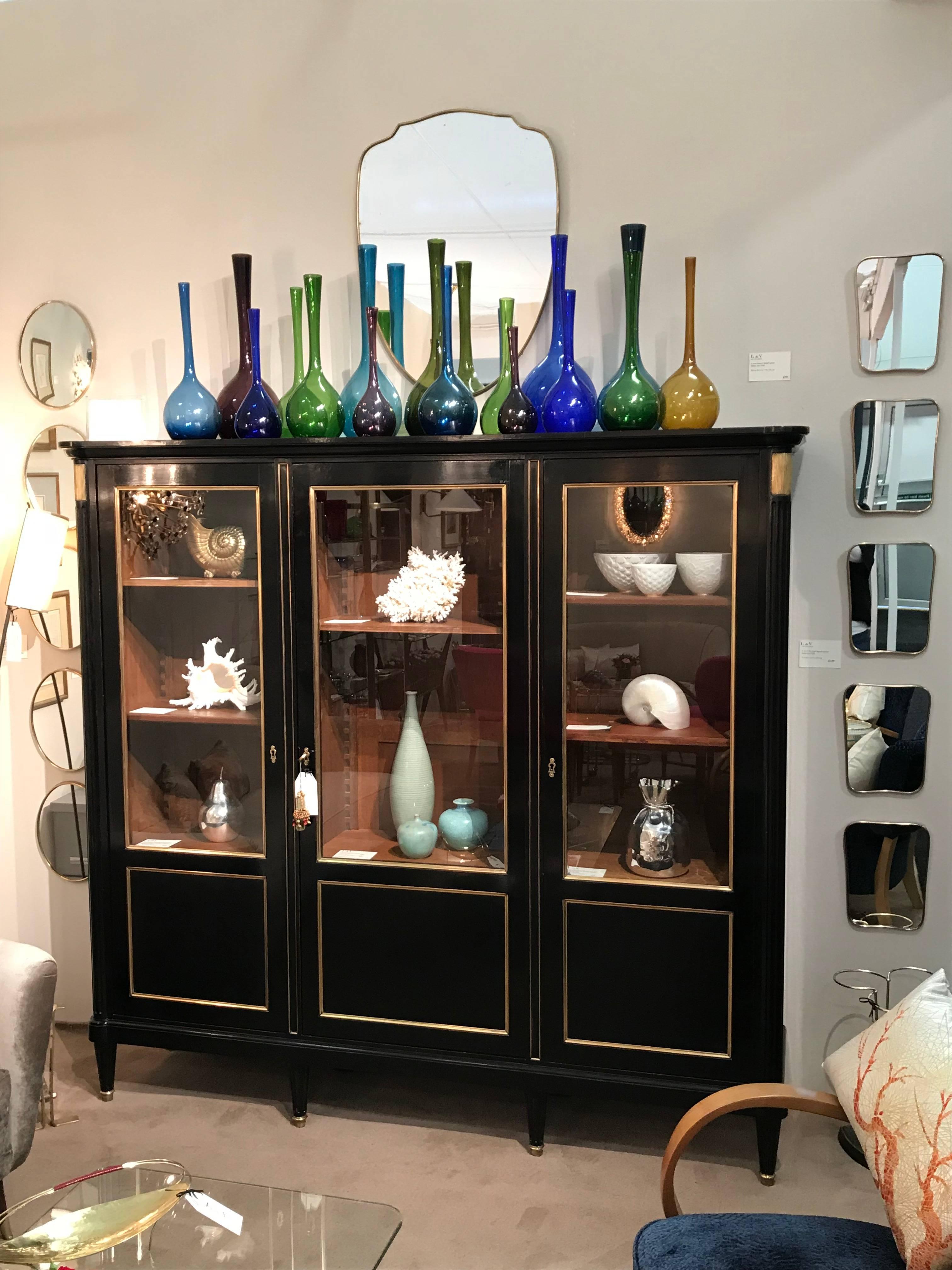 An ebonised oak cabinet with three glazed doors and brass detail
Moveable interior shelves
Items shown in the cabinet are on sold separately.

Measures: Height 68 ½ in / 174 cm
Width 72 ½ in / 185 cm
Depth 17 ¼ in / 43.5 cm.
 