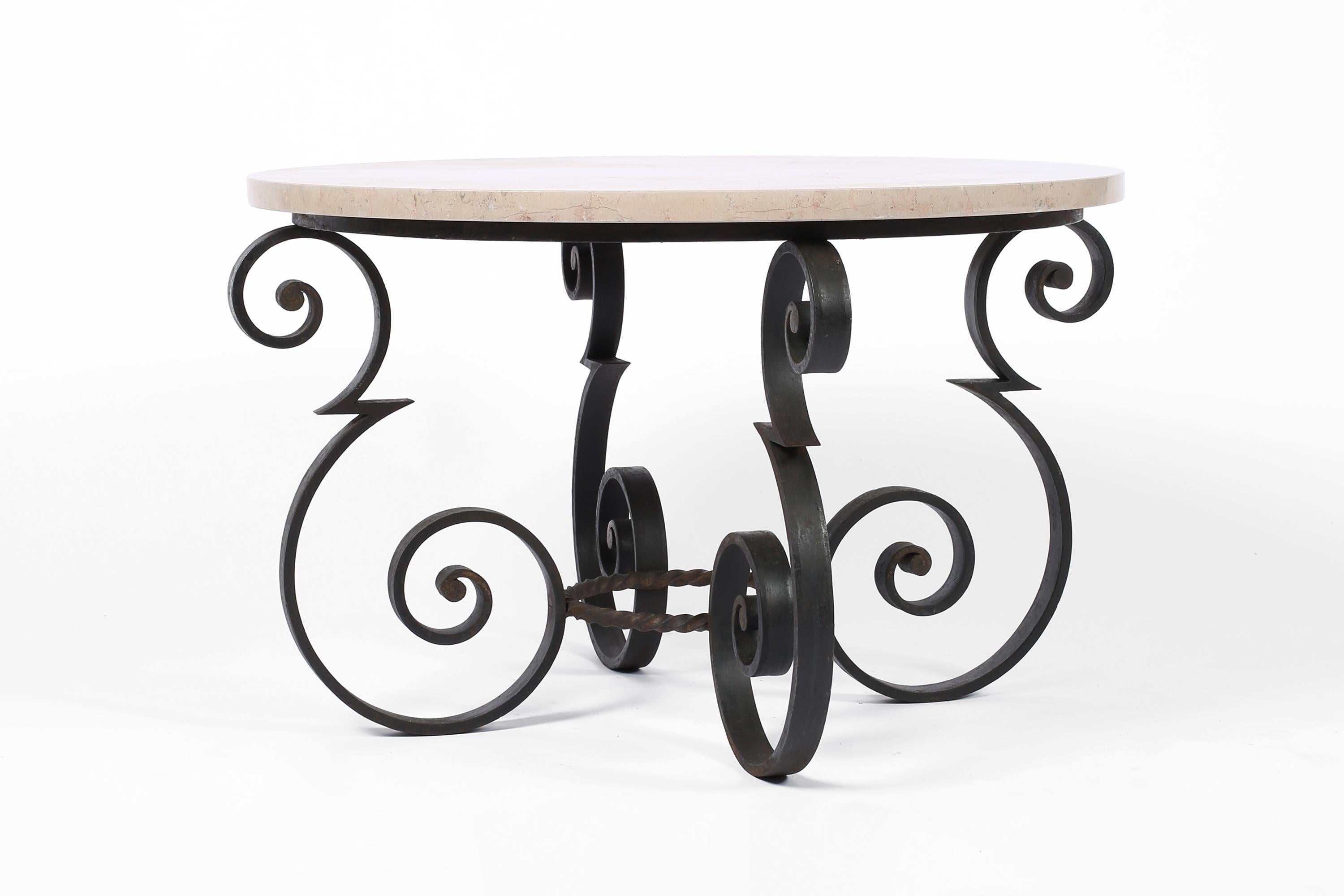 A chic circular forged iron coffee or large side table in the manner of Gilbert Poillerat (1902-1988). The shapely frame with traces of gilding and the original beige/pink hued marble top containing fossil fragments. French, c. 1930s. 