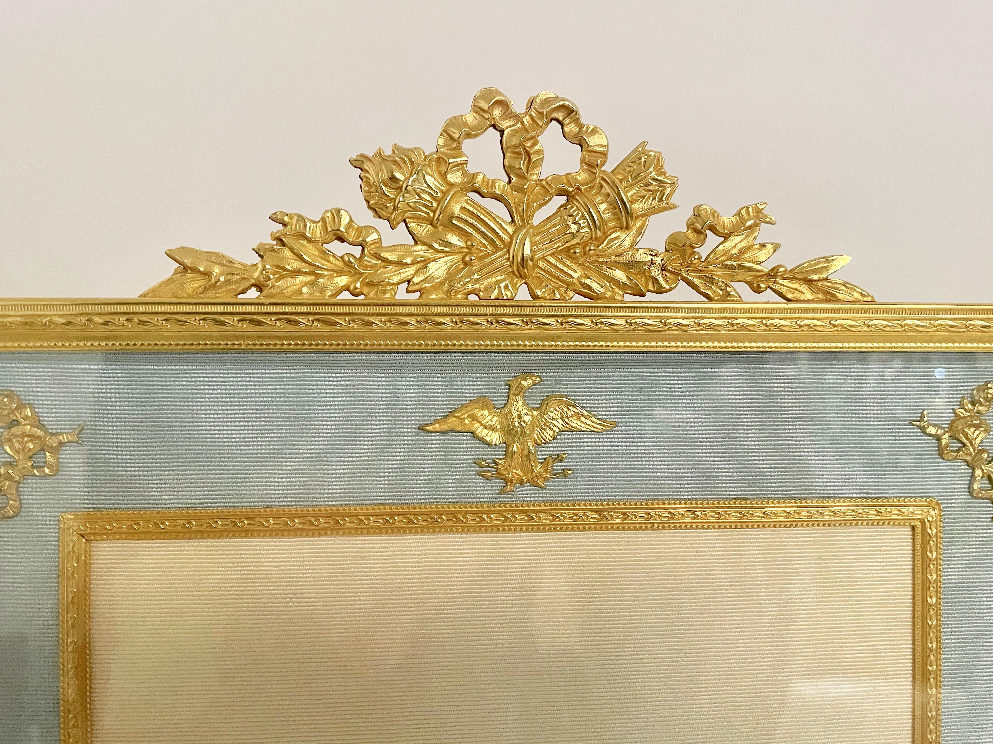 Rectangular gilt bronze photo with arrow and quiver crest. The pale blue silk border with applied classical motifs, French circa 1930, with a later inner silk slip in cream.