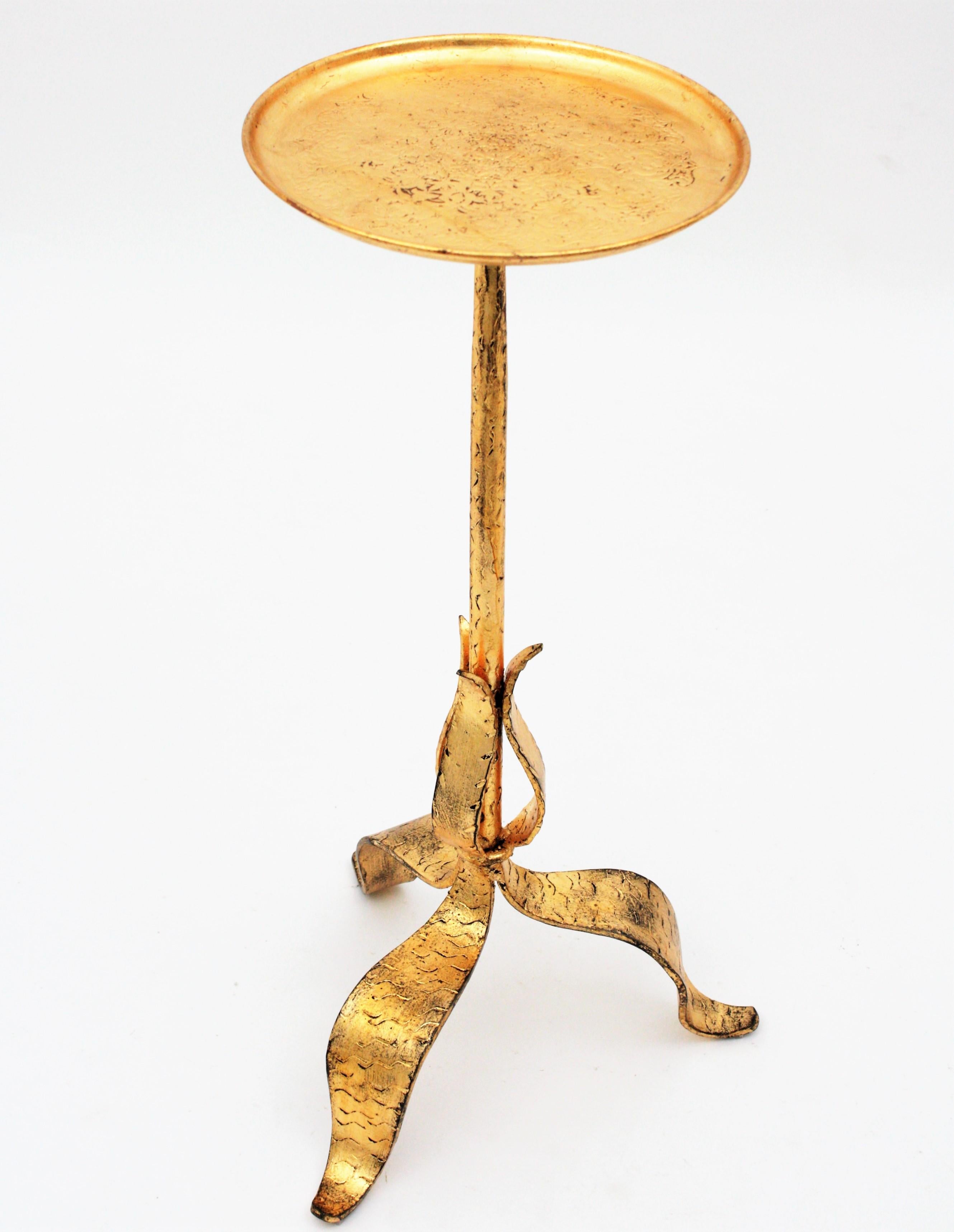 A hand-hammered iron drinks table or stand with a tripod leafed base and filigree adorned round top. France, 1930s.
This handcrafted table has Hammer marks decorating the base and is finished in gold leaf gilt. The top is richly decorated with