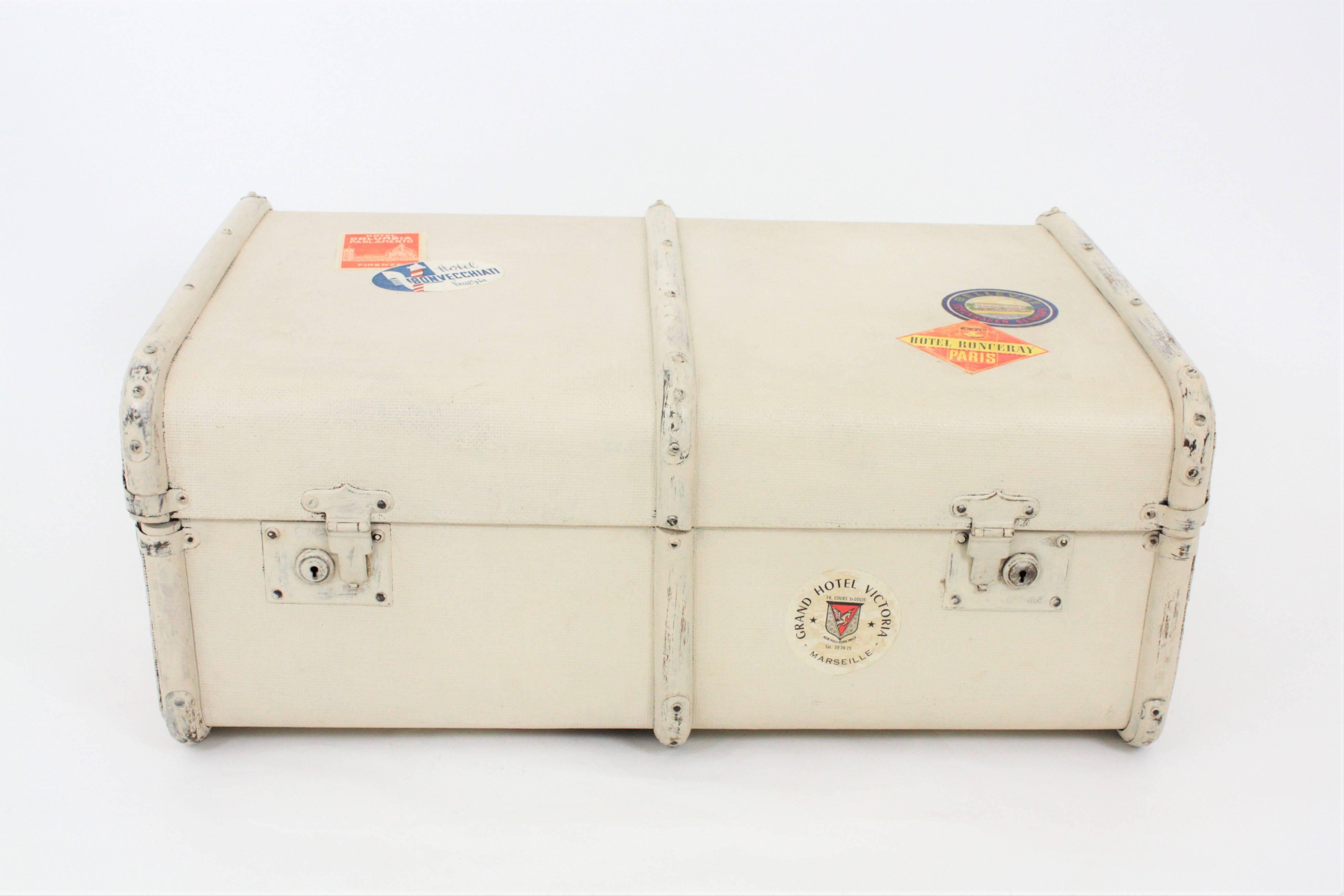 A vintage wood and textile canvas vintage trunk manufactured at the Art Deco period.  It is patinated in ivory color with hotel labels, wooden bars, metal protections and leather handles. Lovely to be used as an storage piece or as a coffee table or