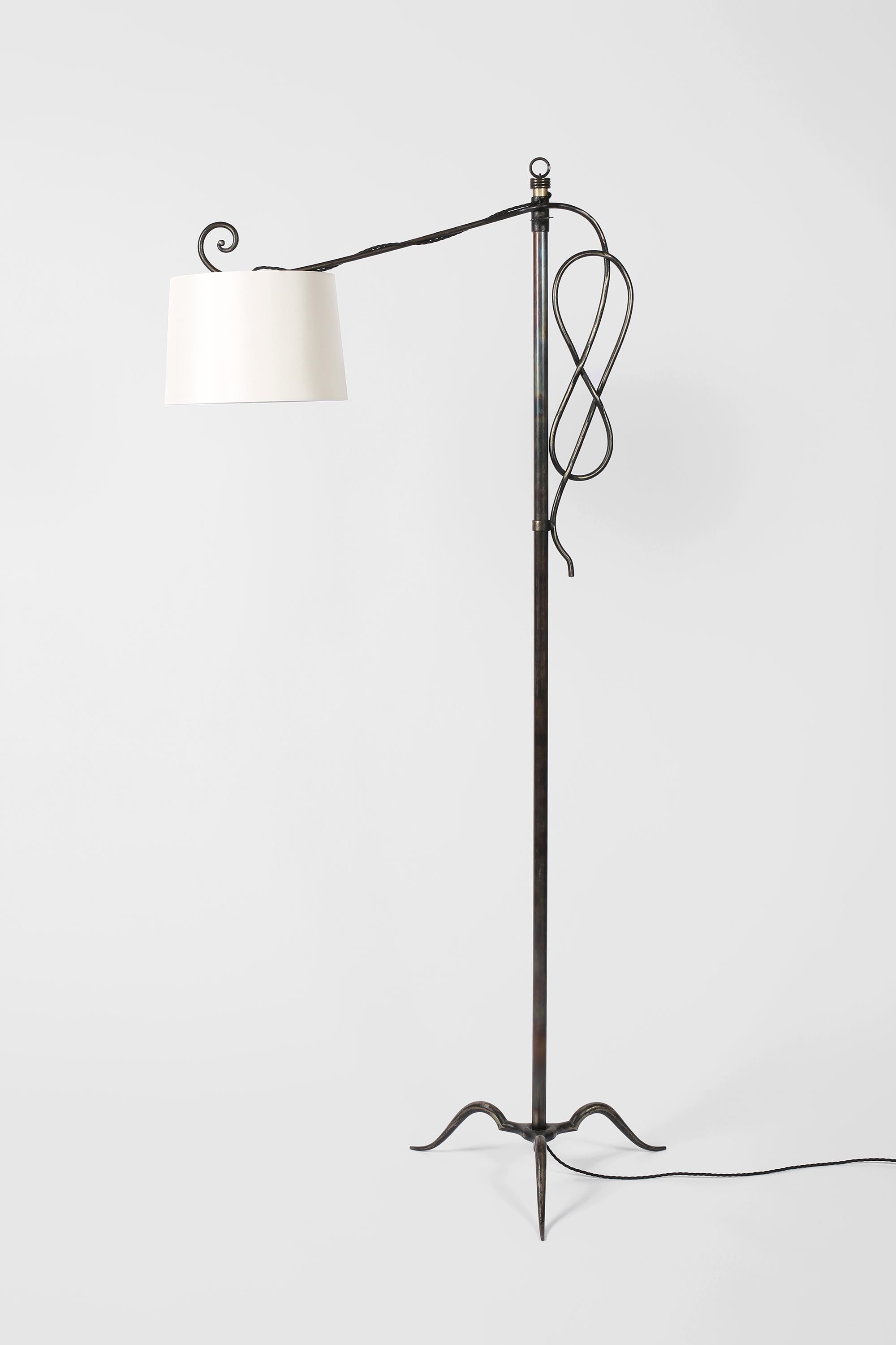 An Art Deco forged iron floor lamp by Michel Zadounaïsky. Featuring a scrolling and knotted height adjustable arm upon a simple stem, with shapely tripod base and decorative ring finial. French, c. 1930s. Supplied with an off-white dupion silk shade.