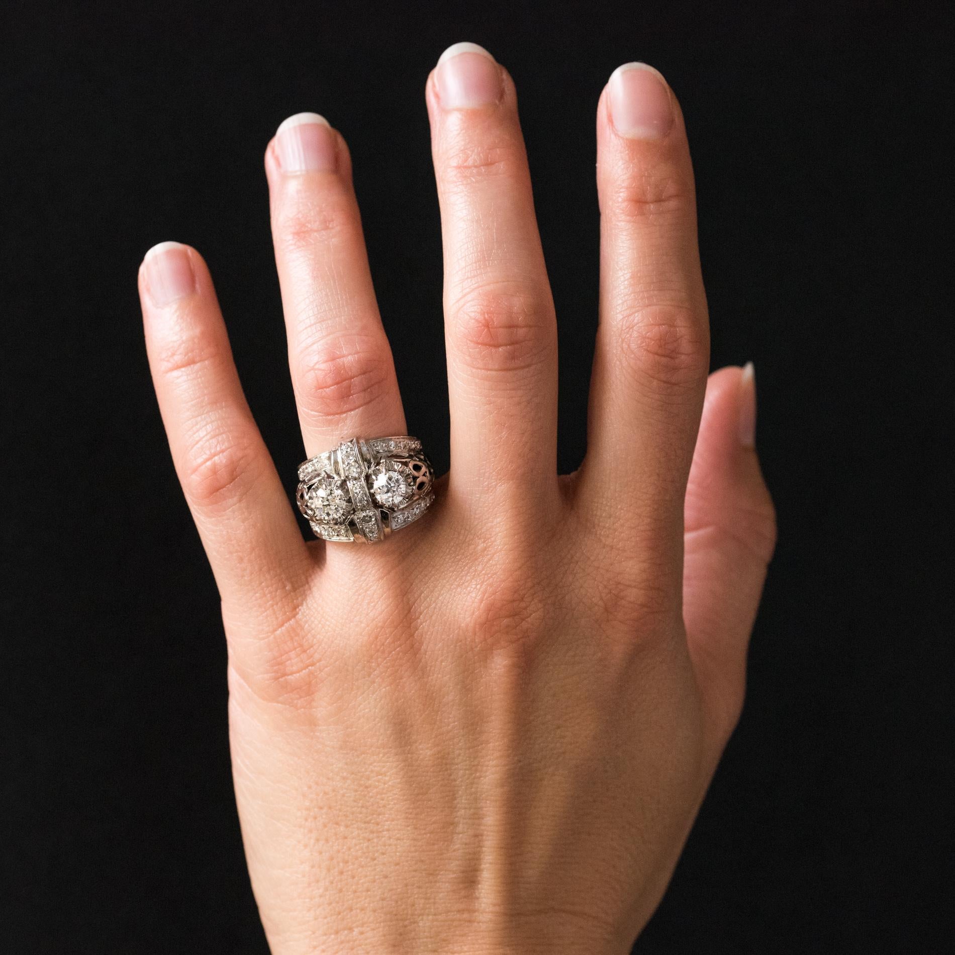 Ring in platinum, mascaron hallmark.
Curved shape, this voluminous antique ring is adorned with 2 antique brilliant- cut diamonds, separated by a kind of knot set with diamonds. On either side, 2 lines of diamonds border the jewel. All on a mounting