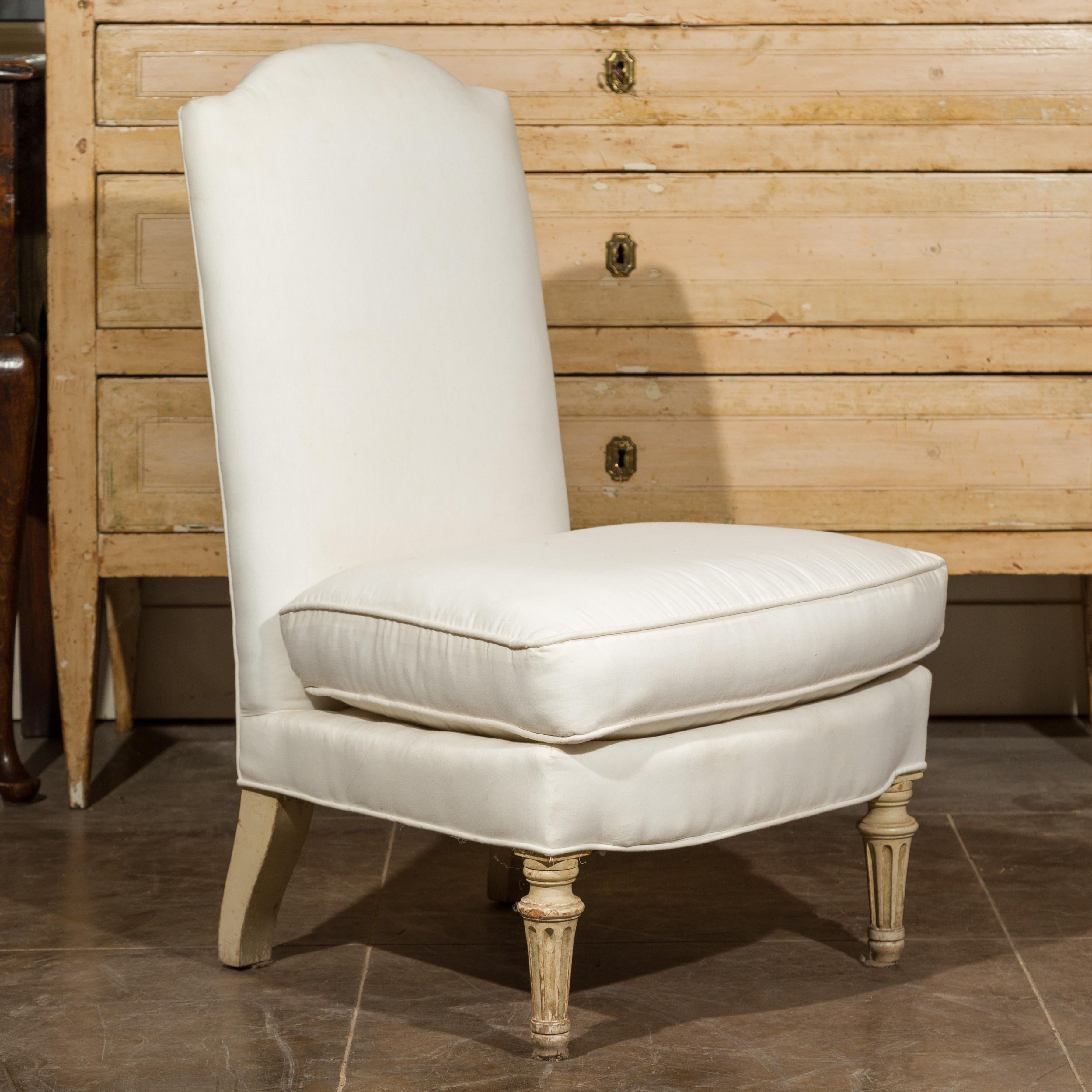 A French slipper chair from the early 20th century, featuring a high straight rectangular backrest with a crossbow-shaped top, covered with a new custom smooth white muslin upholstery. The seat also features a loose fitting trapezoidal cushion. Born