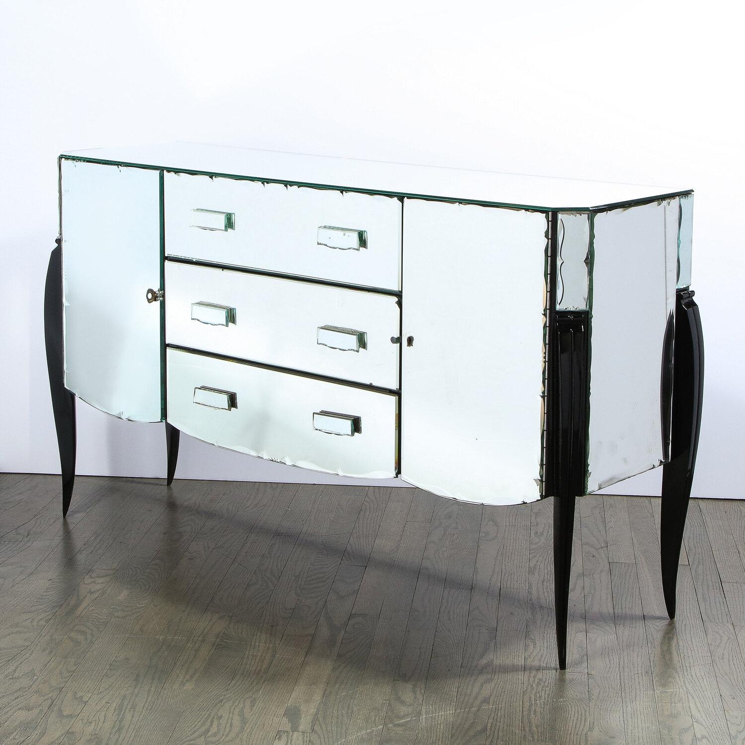 This elegant Art Deco cabinet was realized in France, circa 1940. It features a three center drawers with rectilinear pulls; two side doors that open to reveal shelved compartments; a scalloped bottom; and cabriolet legs in ebonized walnut.