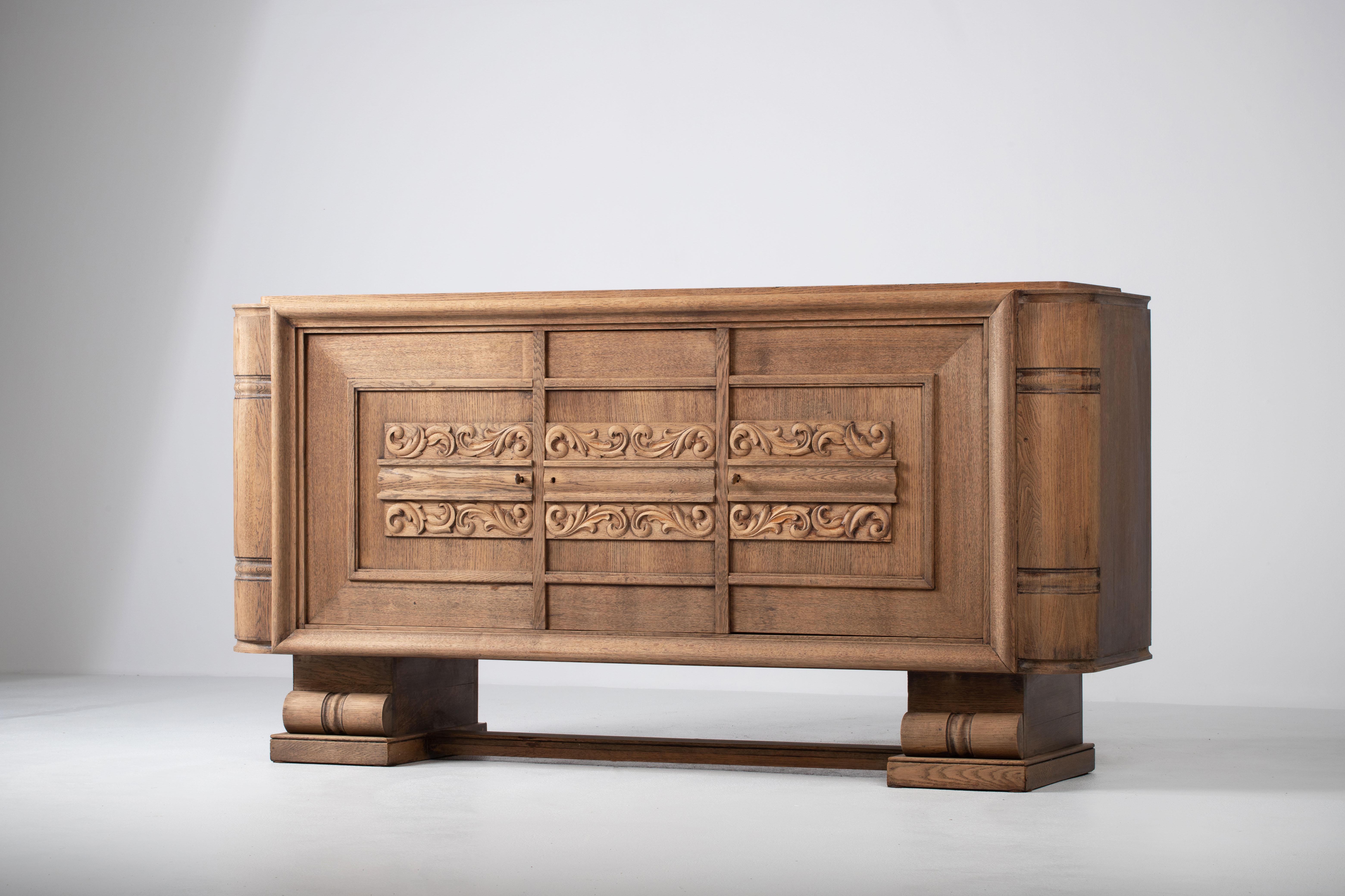 Composition d'une grandeur stoïque, cette crédence française des années 1940 articule un langage de retenue sculpturale et de monumentalité tranquille. La façade se déploie en trois compartiments encadrés par une géométrie inébranlable, chaque porte
