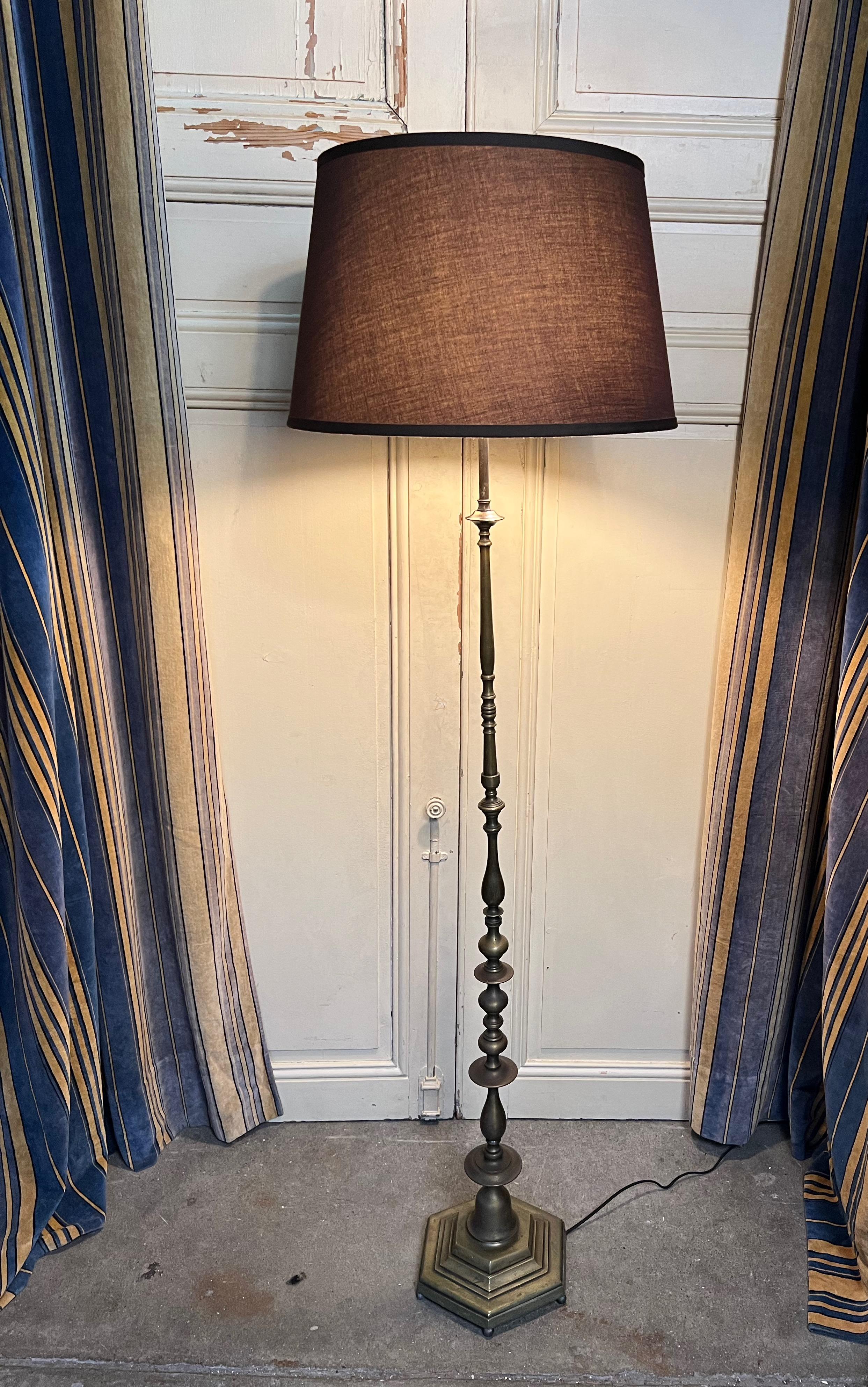 This French 1940s floor lamp features a cast hexagonal base resting on ball feet, providing stability and elegance. The stem is composed of turned and cast bronze pieces that gracefully taper towards the top. The hand-patinated, oil rubbed brass