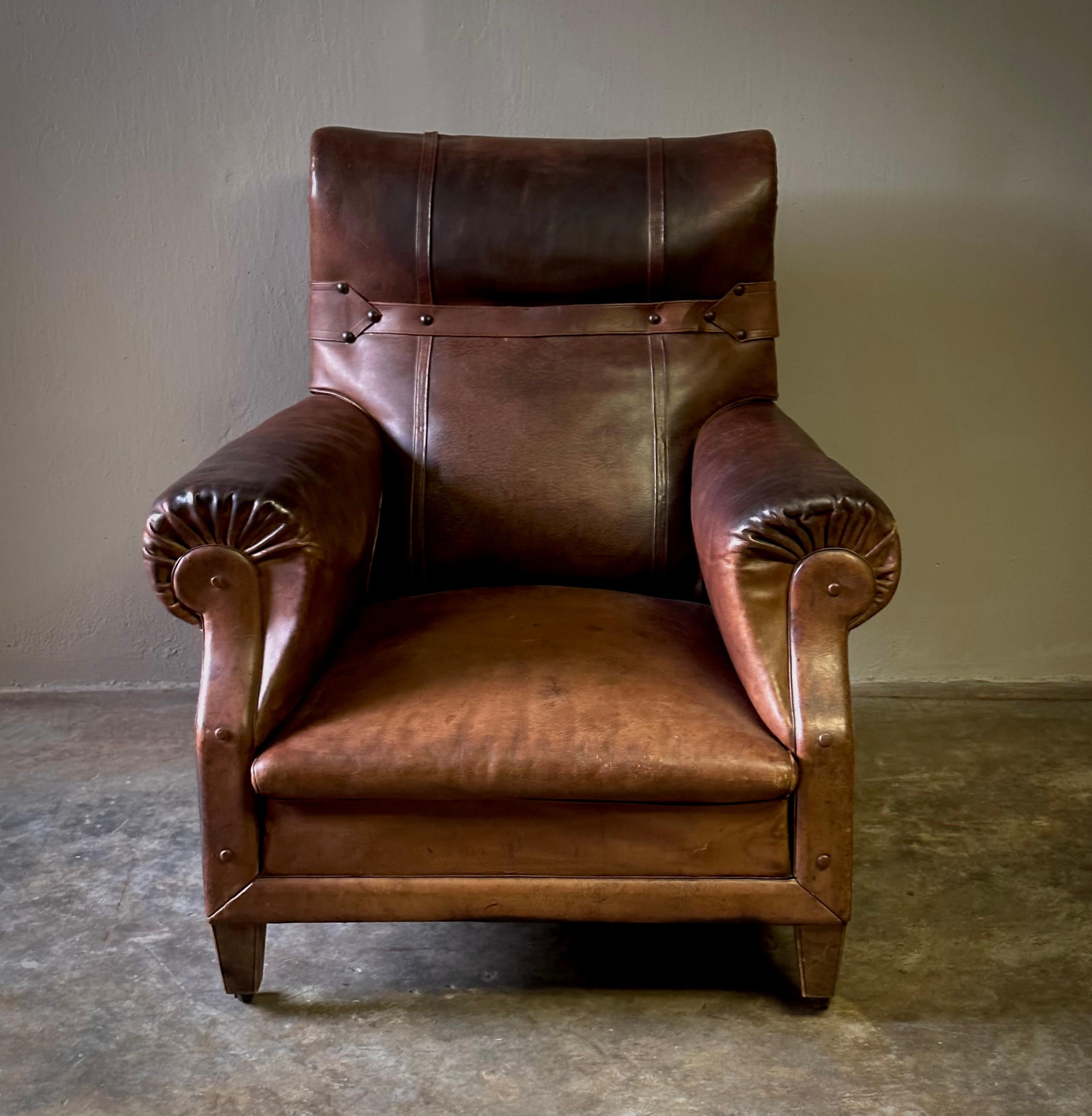 French 1940s chestnut leather semi-winged arm chair with industrial metal studded strap accent. Beautifully aged leather and unique detailing give this handsome piece a clubby, sporty feel. 

France, circa 1940

Dimensions: 35.4W x 35.4D x 37.8H