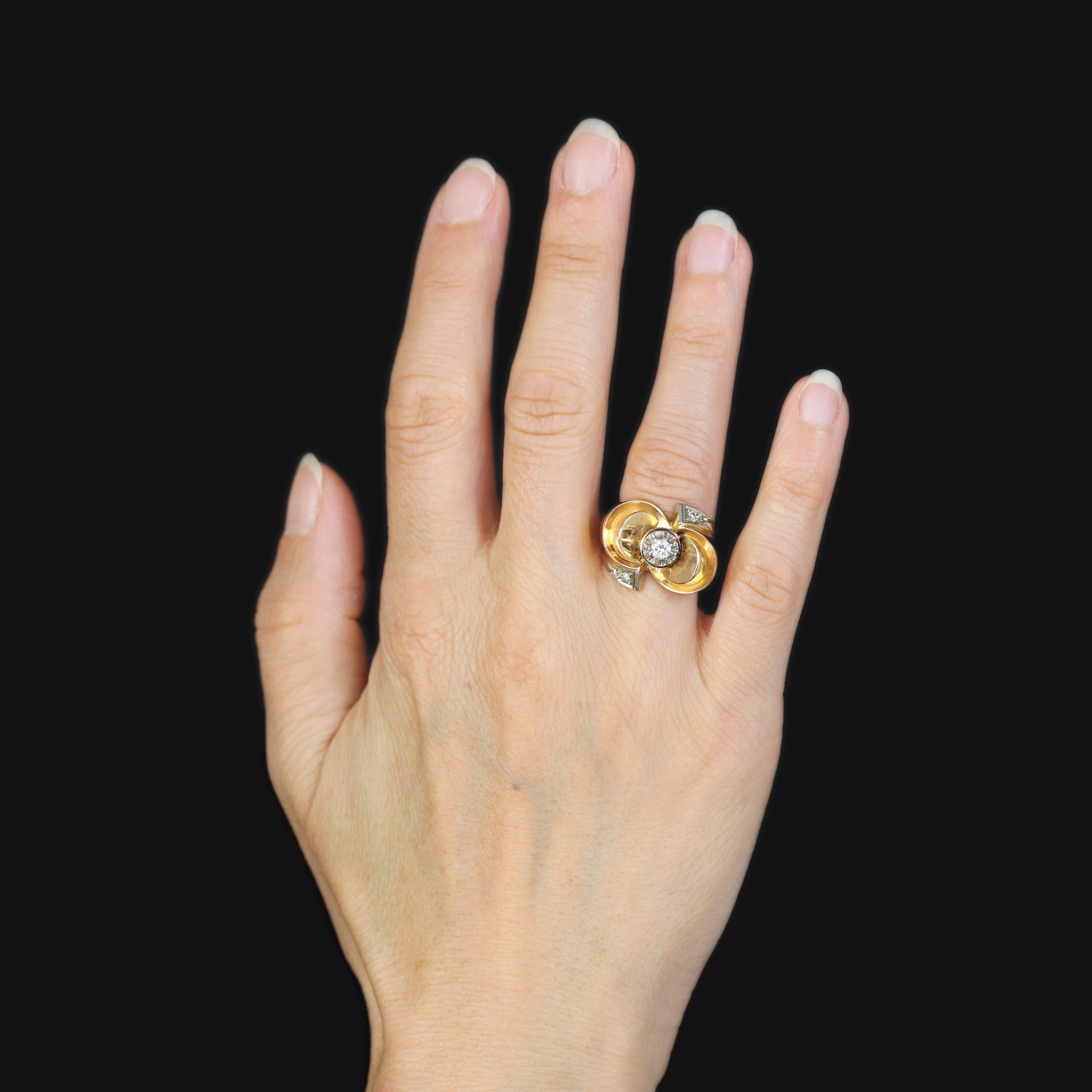 Bague en or rose 18 carats, poinçon tête d'aigle, et en platine, poinçon tête de chien.
Bague rétro, sa monture forme un important nœud décoré au centre d'un diamant intermédiaire taille brillant retenu par des griffes en platine. De chaque côté de