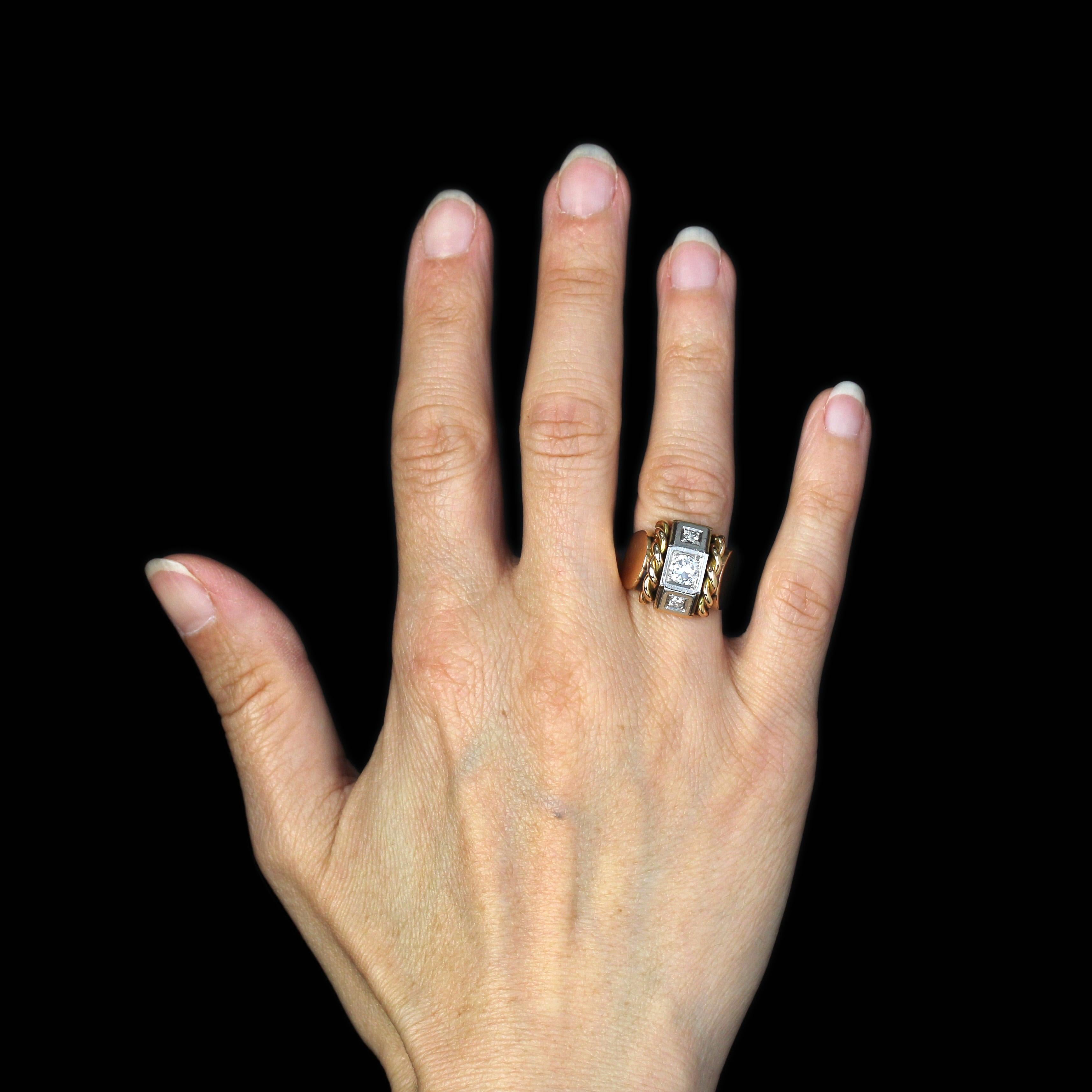 Bague en or jaune 18 carats, poinçon tête d'aigle, et en platine, poinçon tête de chien.
Bague Tank, elle est ornée sur le dessus de trois diamants taille brillant sur des motifs géométriques. Des deux côtés, un cordon est placé avant le départ de