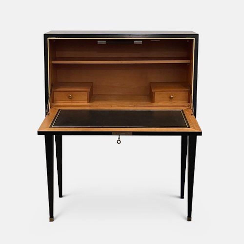 An elegant 1940s ebonized desk attributed to Jacques Adnet. Set on four tapered legs, the front drops down to reveal a writing desk with cherry wood interior, lined tooled leather insert, interior light, two drawers and a shelf. The piece is set off