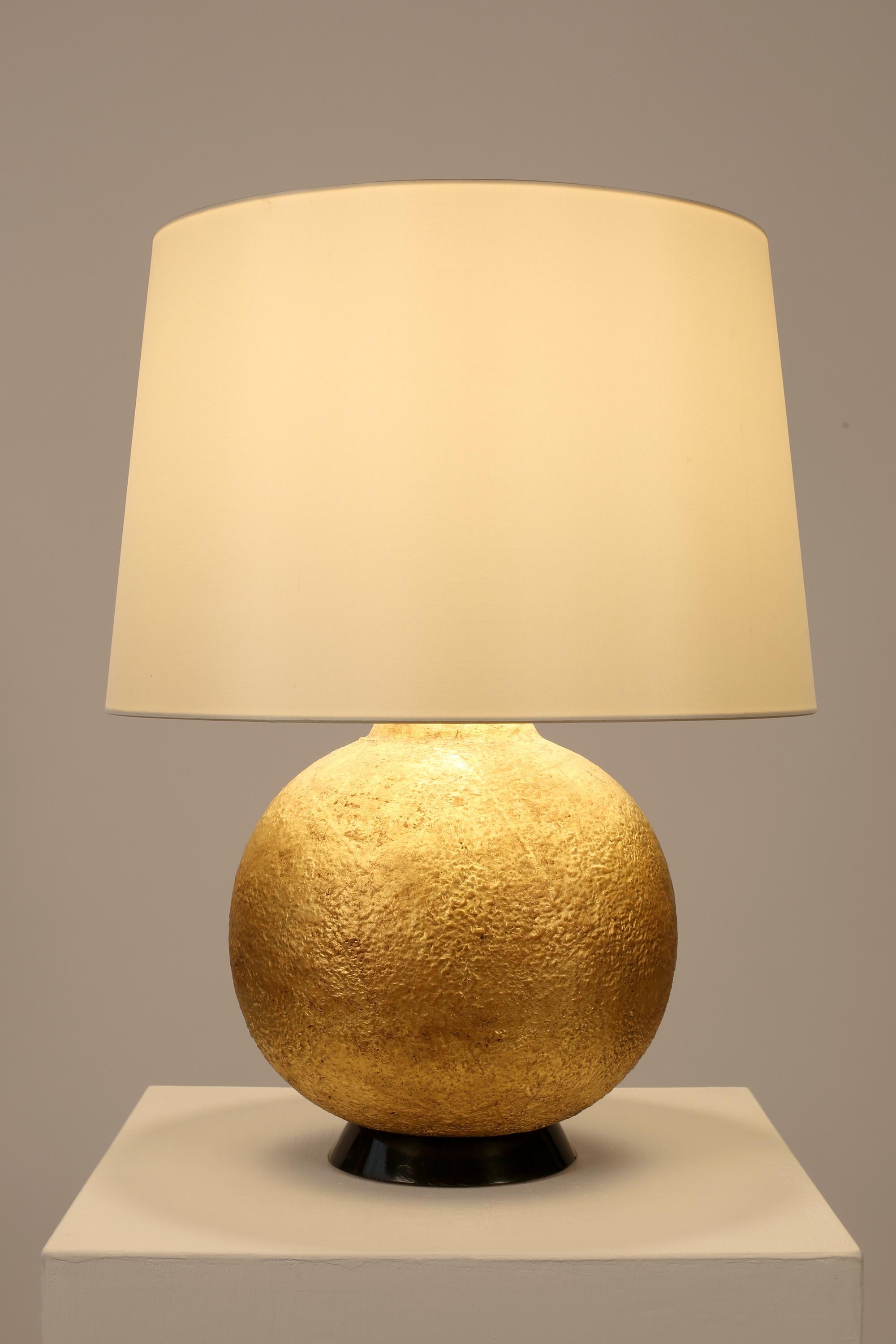 Grande lampe de table en plâtre doré de forme ronde texturée, reposant sur une base en bois tourné et laqué noir. Le matériau et la finition font écho au travail d'Alberto Giacometti ou de Jean-Michel Frank. Français, c. 1940. Livré avec un