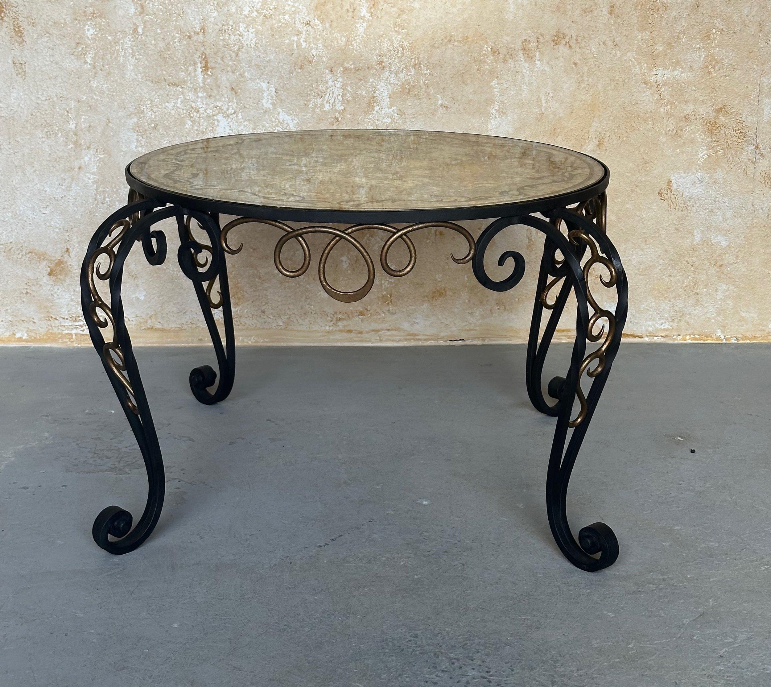 An interesting French 1940s iron coffee table with a decorative reverse painted mirror top. The elegantly scrolled base has recently been refinished in a matte black paint with hand-applied gold accents that contrast beautifully with the reverse