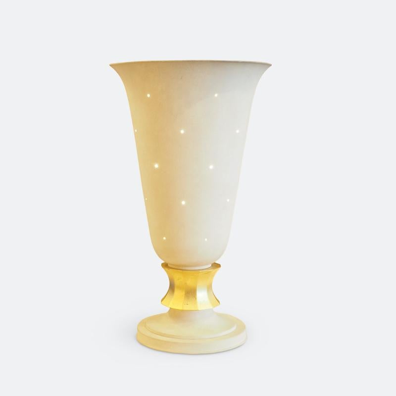 Une grande lampe de table décorative des années 1940 attribuée à Genet & Michon. Le corps en métal peint à la main de couleur crème se termine par une tige néoclassique en feuille d'or dorée. Le corps est ponctué de petites ouvertures qui laissent