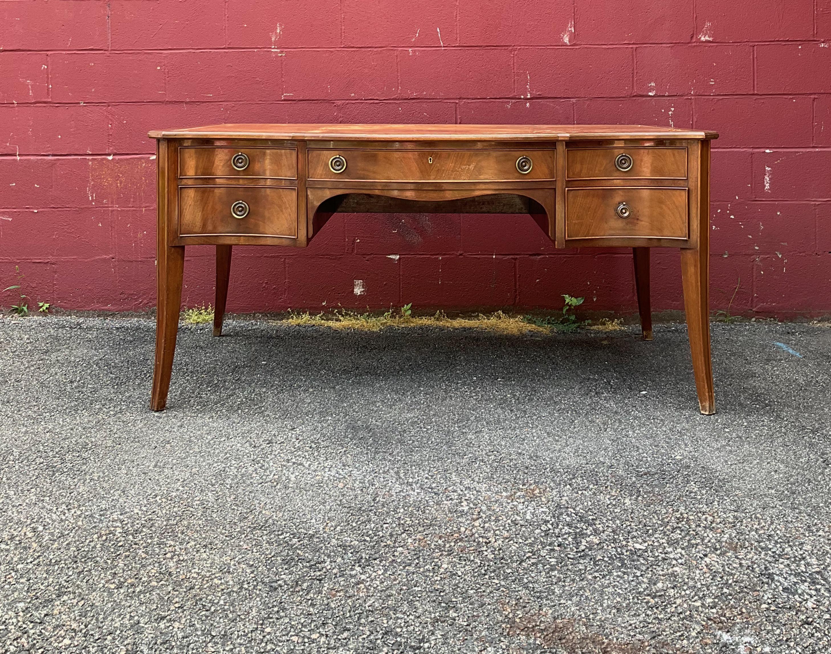 Unusual and handsome mahogany French desk from the 1940s-1950s with a distressed leather top. There is one large central drawer as well as two side drawers on either side and the back of the desk is finished so it can float in a room. The tooled