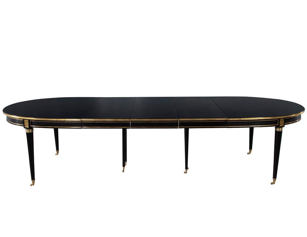 French 1940s Maison Jansen Dining Table in Polished Black with Brass Detailing. France, circa 1940s. Featuring high gloss polished black lacquered finish with all original brass ornaments. Table features 3 leaves with hideaway dropdown legs to