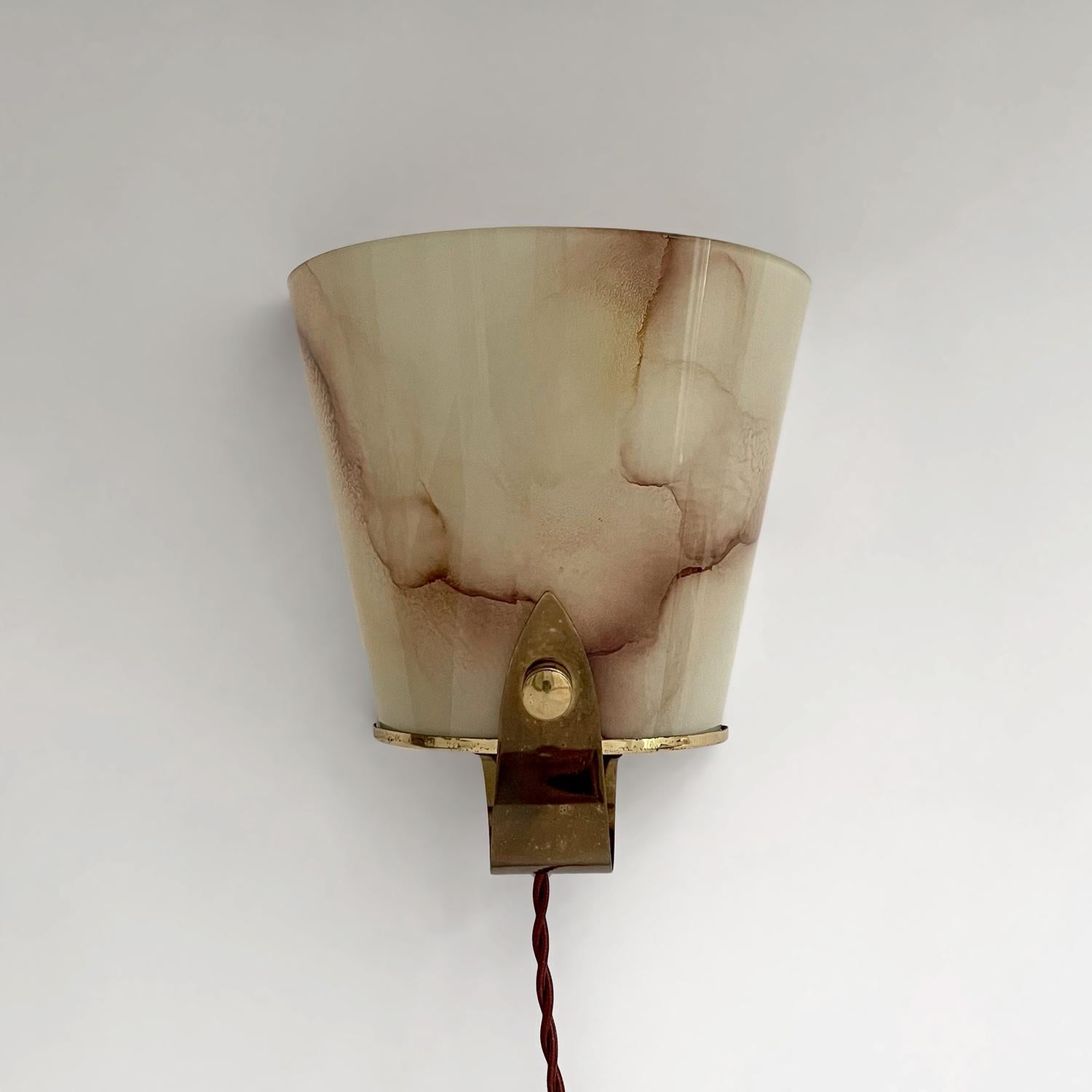 French marbled glass & brass sconce
France, 1940’s
Delicate semicircular marbled glass shade rests within sculpted aged brass frame
Light surface markings 
Illuminates light beautifully 
Patina from age and use
Newly rewired
Single socket candelabra