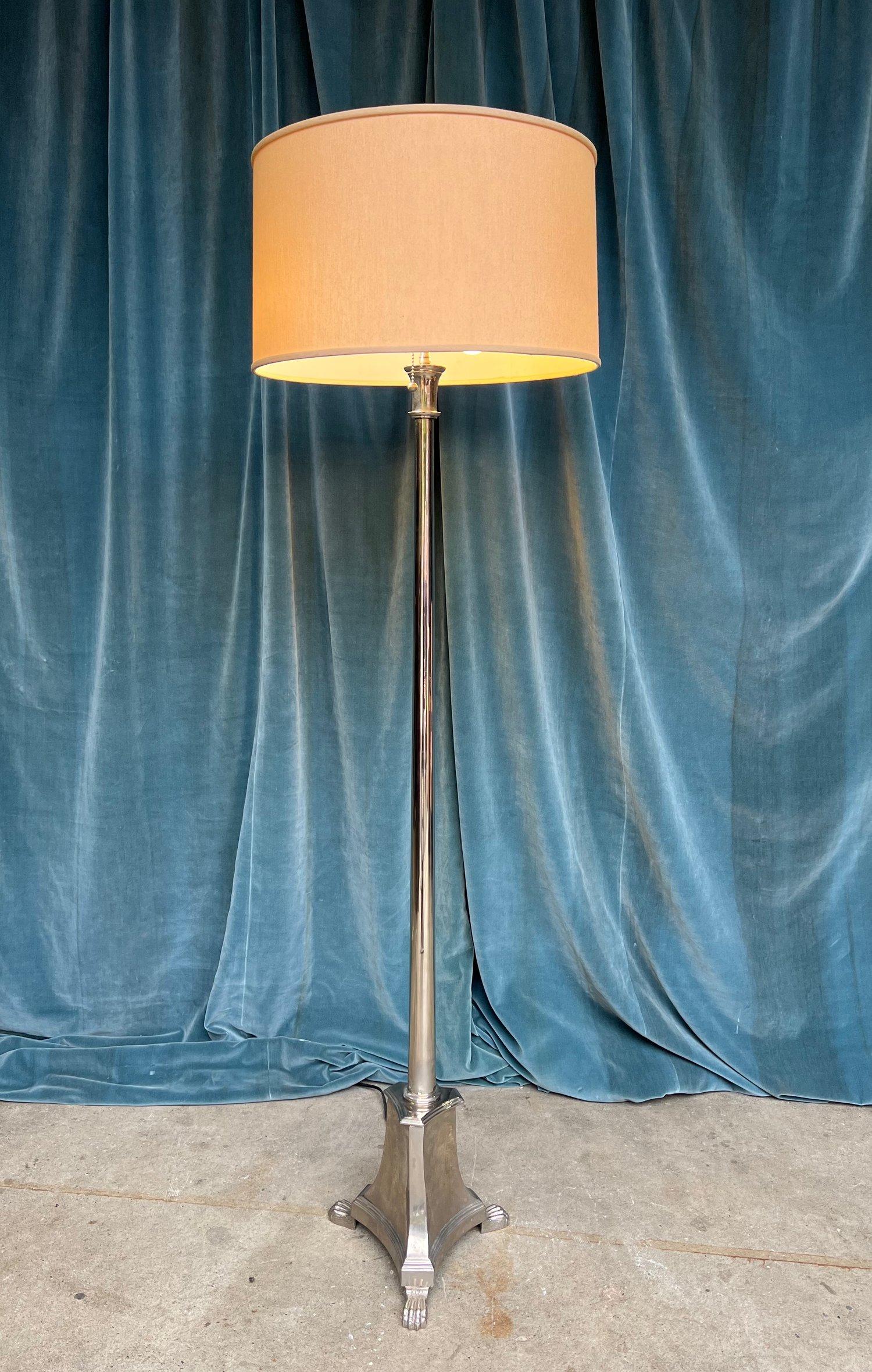 A French 1940s Neoclassical style floor lamp in a polished nickel finish ready to illuminate your space with style and grace. It features a footed triangular base that not only provides stability but also adds an element of elegance. The gracefully
