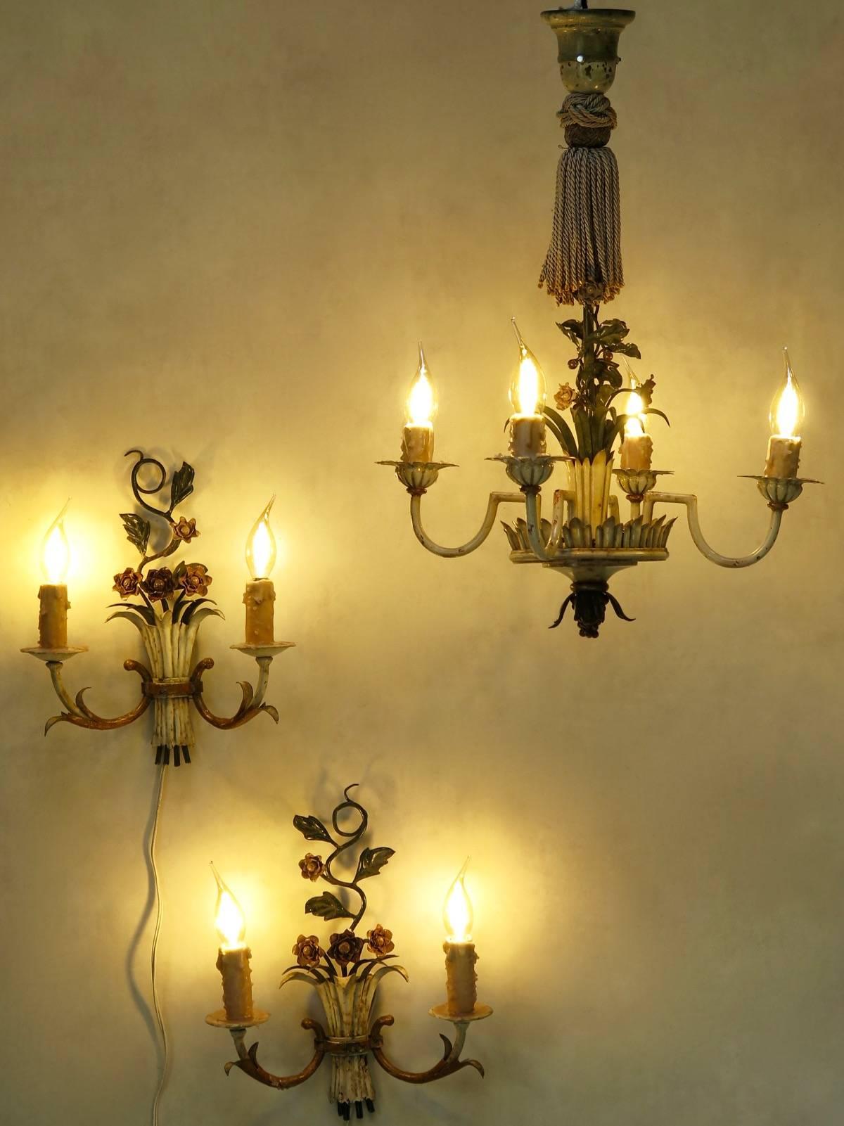 Charming set comprised of a chandelier and two sconces. The structure is of painted iron, with a delicate floral decor, and pointy leaves. The chandelier has a large twisted silk tassel at the top, and four lights.

Dimensions provided below are