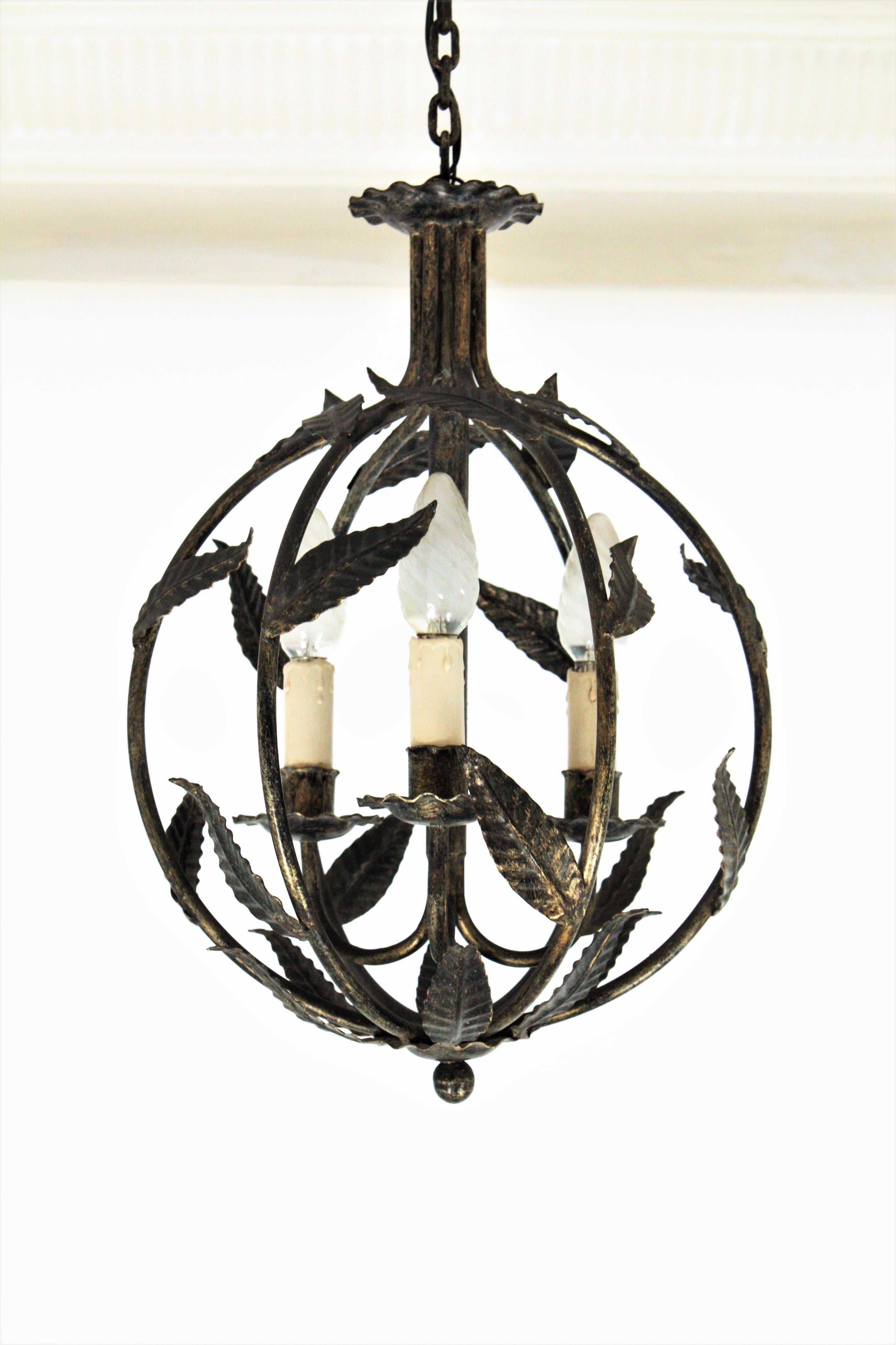 Eye-catching three-light wrought iron globe pendant or lantern with leaf motif design, France, 1940s.
This chandelier features a patinated iron globe shaped structure decorated with leaves and gilt accents. It hangs from a chain holded by a