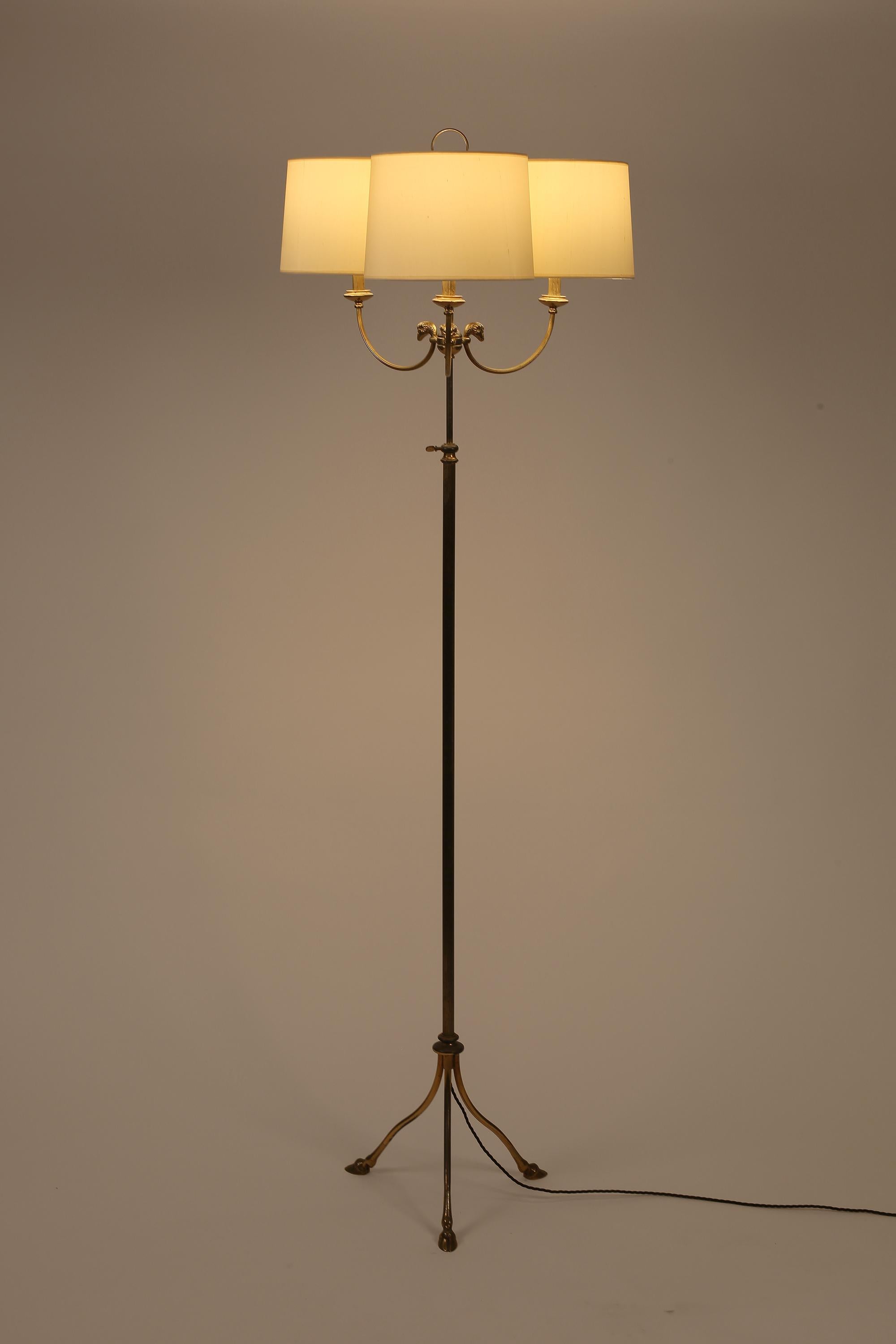 Vergoldetes Messing, höhenverstellbare dreiköpfige Stehlampe im klassischen Geschmack. Drei maßgeschneiderte, cremefarbene Seidenschirme sitzen auf geformten Armen, die mit Widderkopfdetails verziert sind, über einem schlichten, geriffelten Stiel